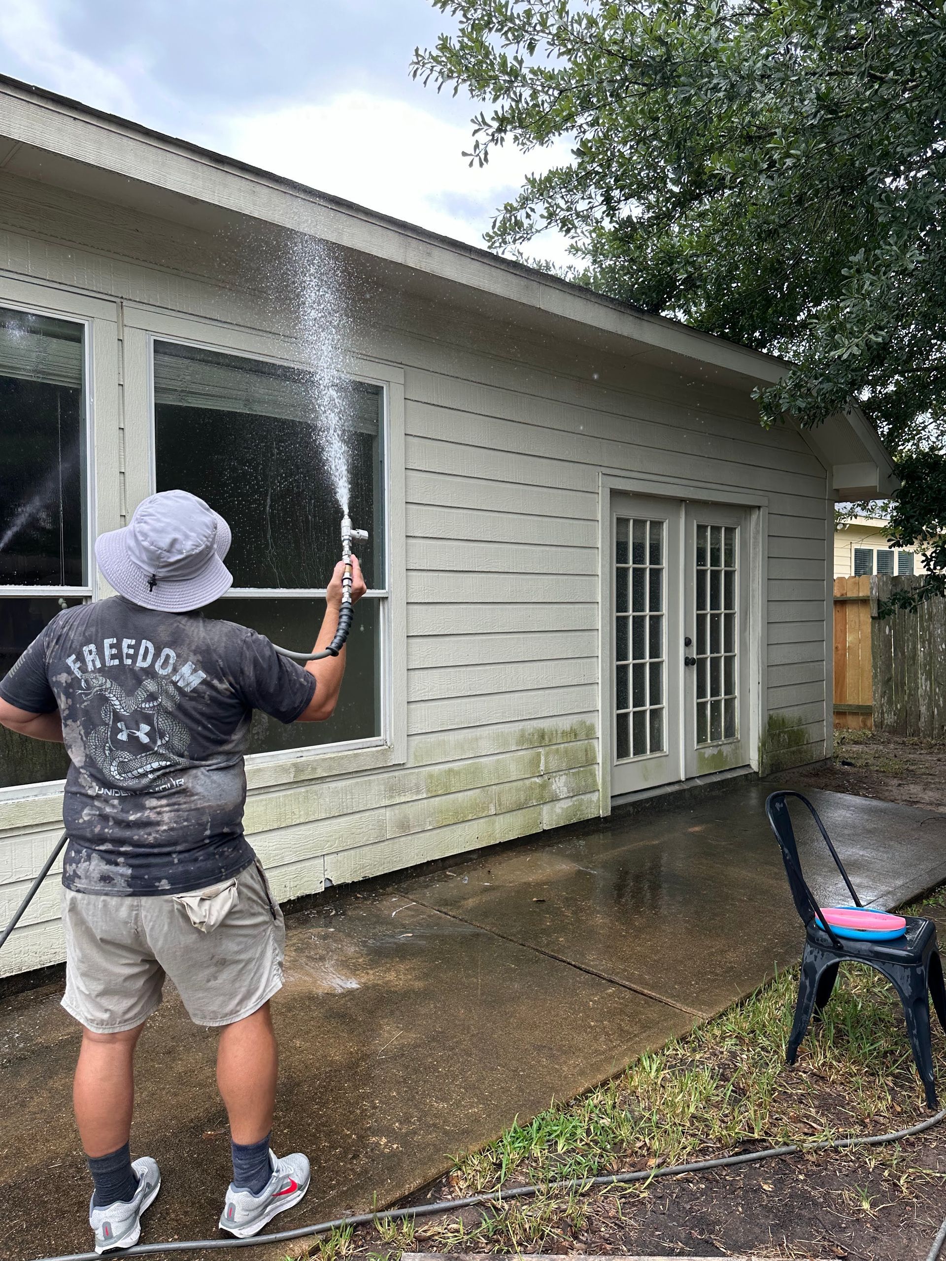 Person spraying water on a house exterior with a hose on a wet driveway