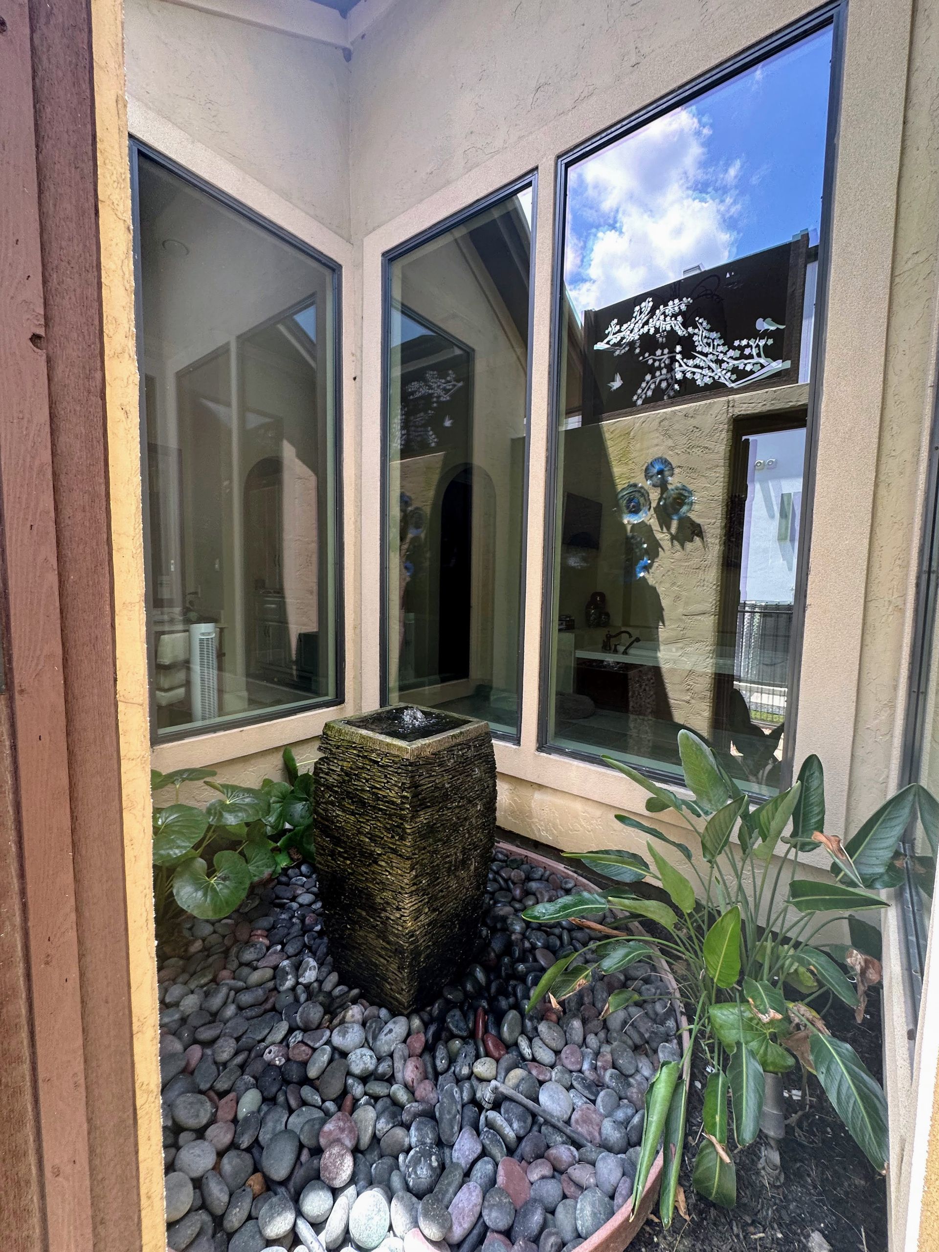 Corner courtyard with a small fountain, white walls, reflective windows, and lush potted plants.