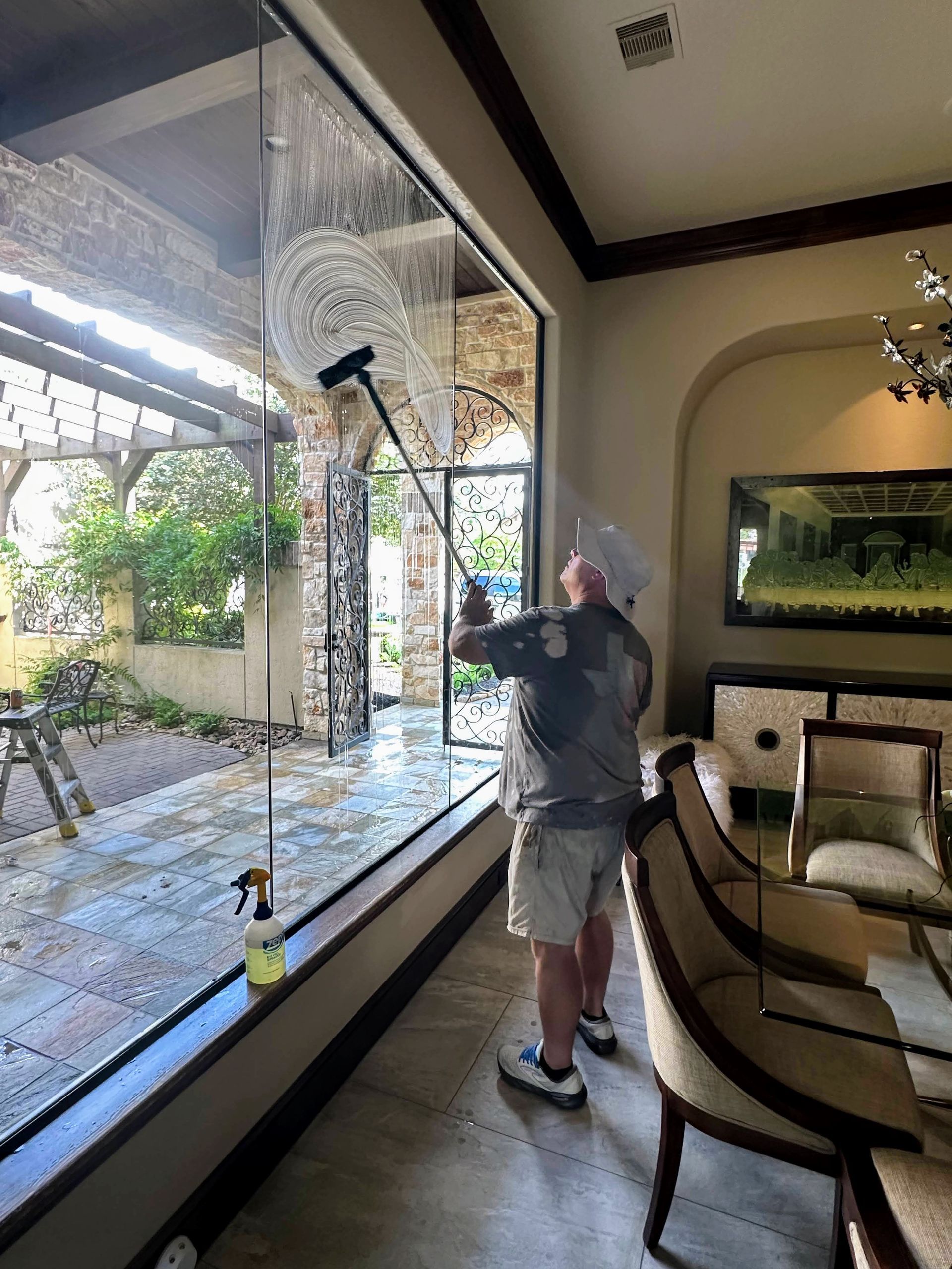 Person using a window washer inside a living room, cleaning large glass doors overlooking a patio.