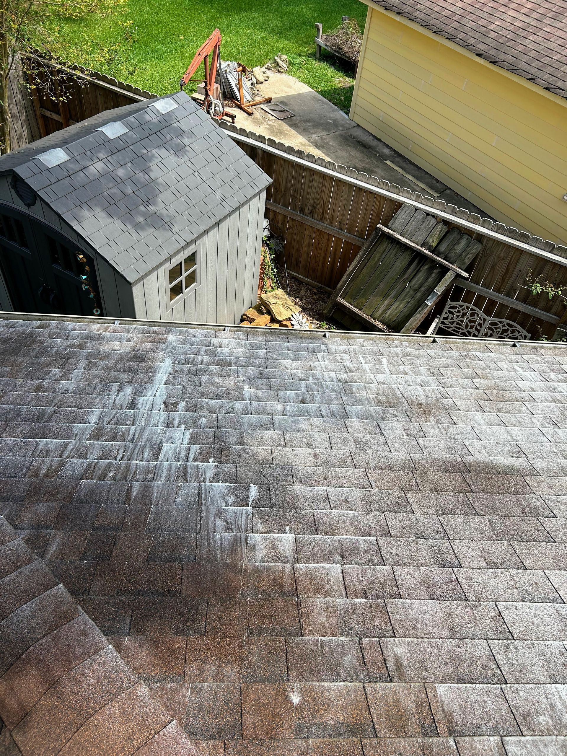 Rooftop view of a backyard with a small shed, fence, and person working near a crane.