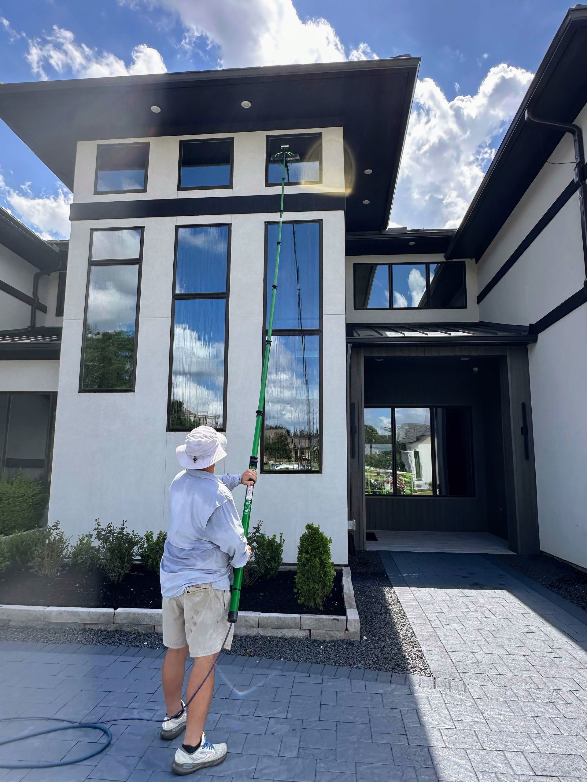 Person standing outside a modern white house with tall windows, pointing toward the facade.