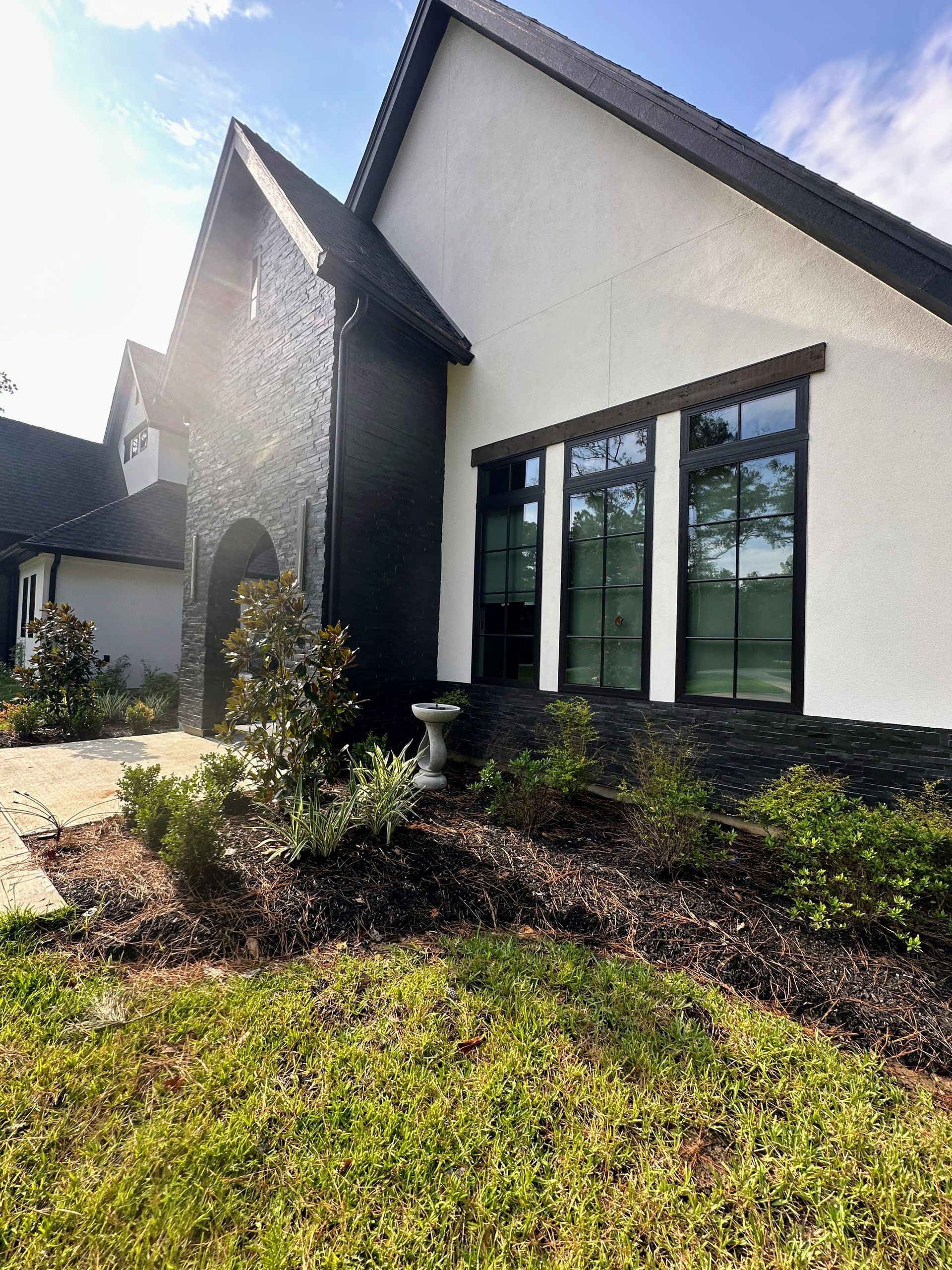 Modern house exterior with white walls, dark trim, large windows, and landscaped front yard