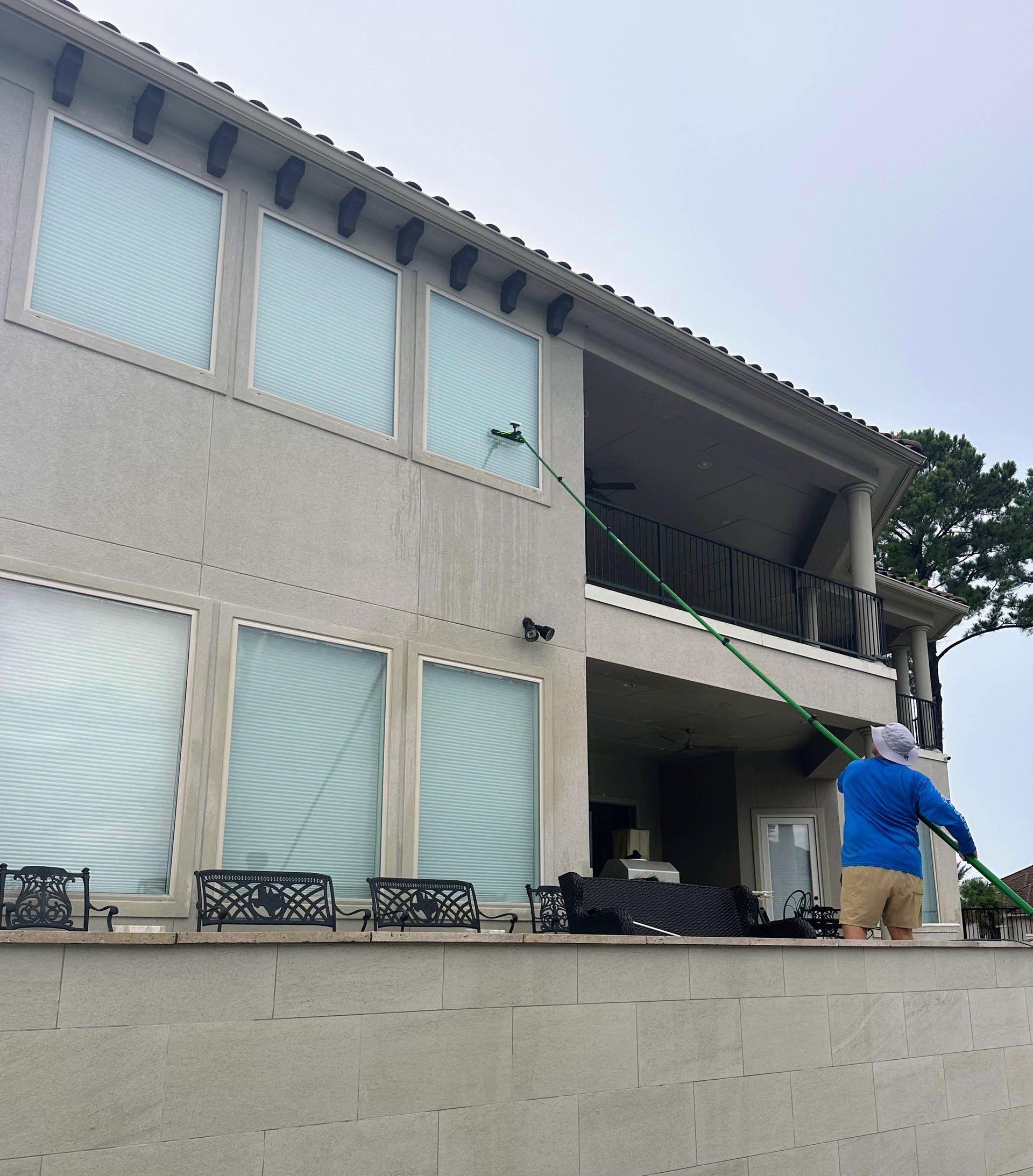 Two-story house with draped windows, a person in blue on the porch, and a green hose across the balcony