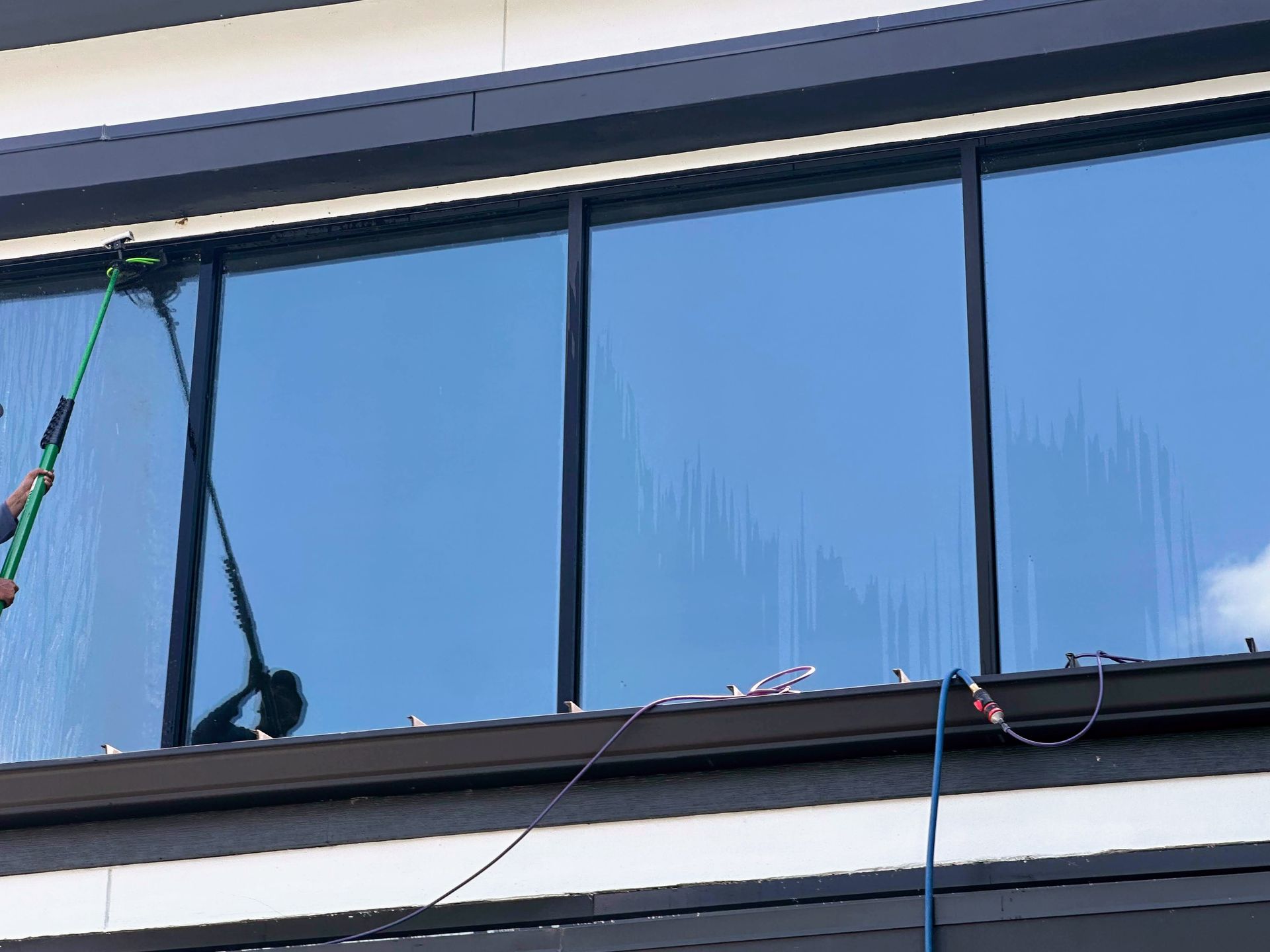 A building window being cleaned from outside with a long pole against blue glass panels.
