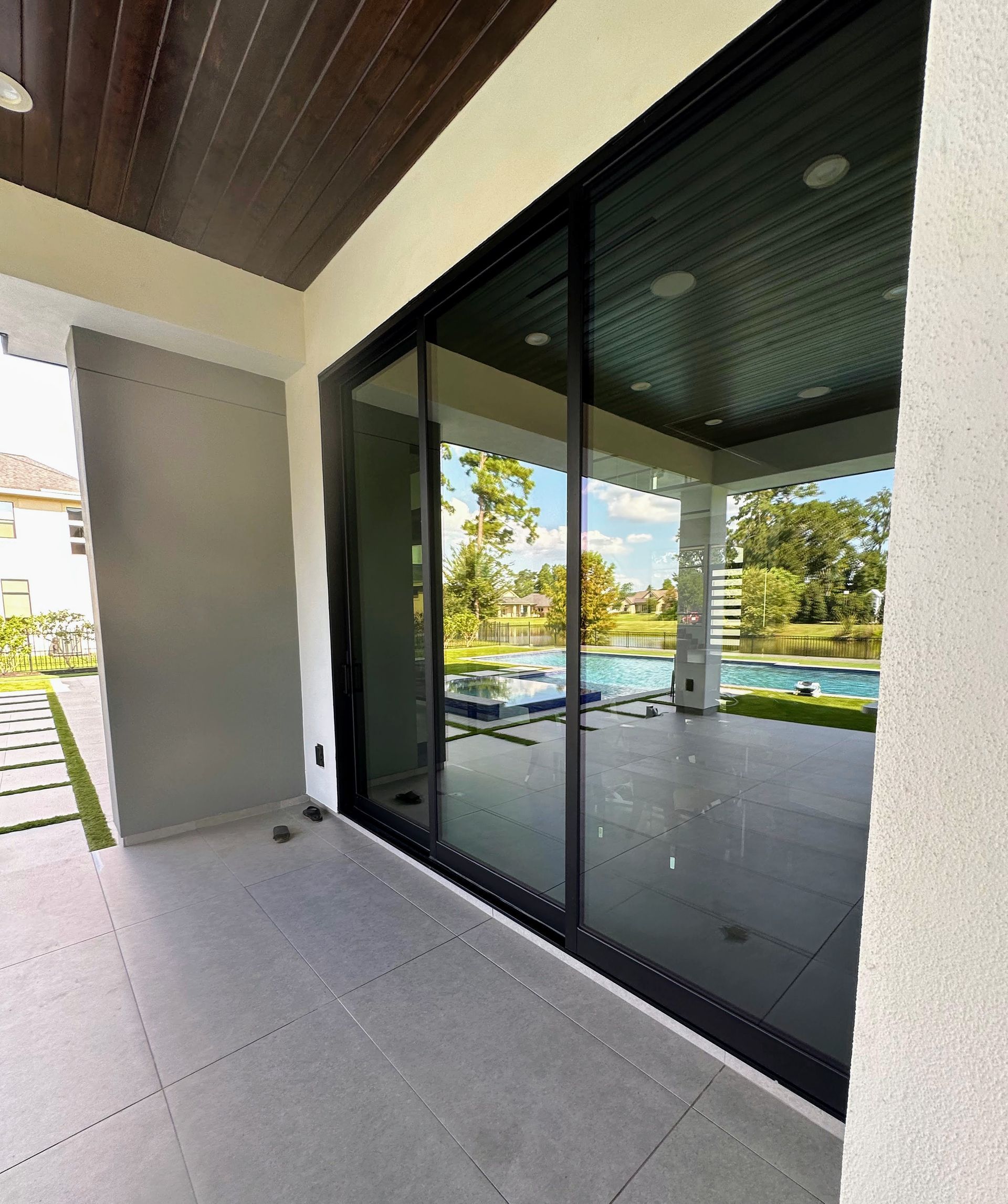 Covered patio with large black sliding glass doors overlooking a pool and palm-lined yard