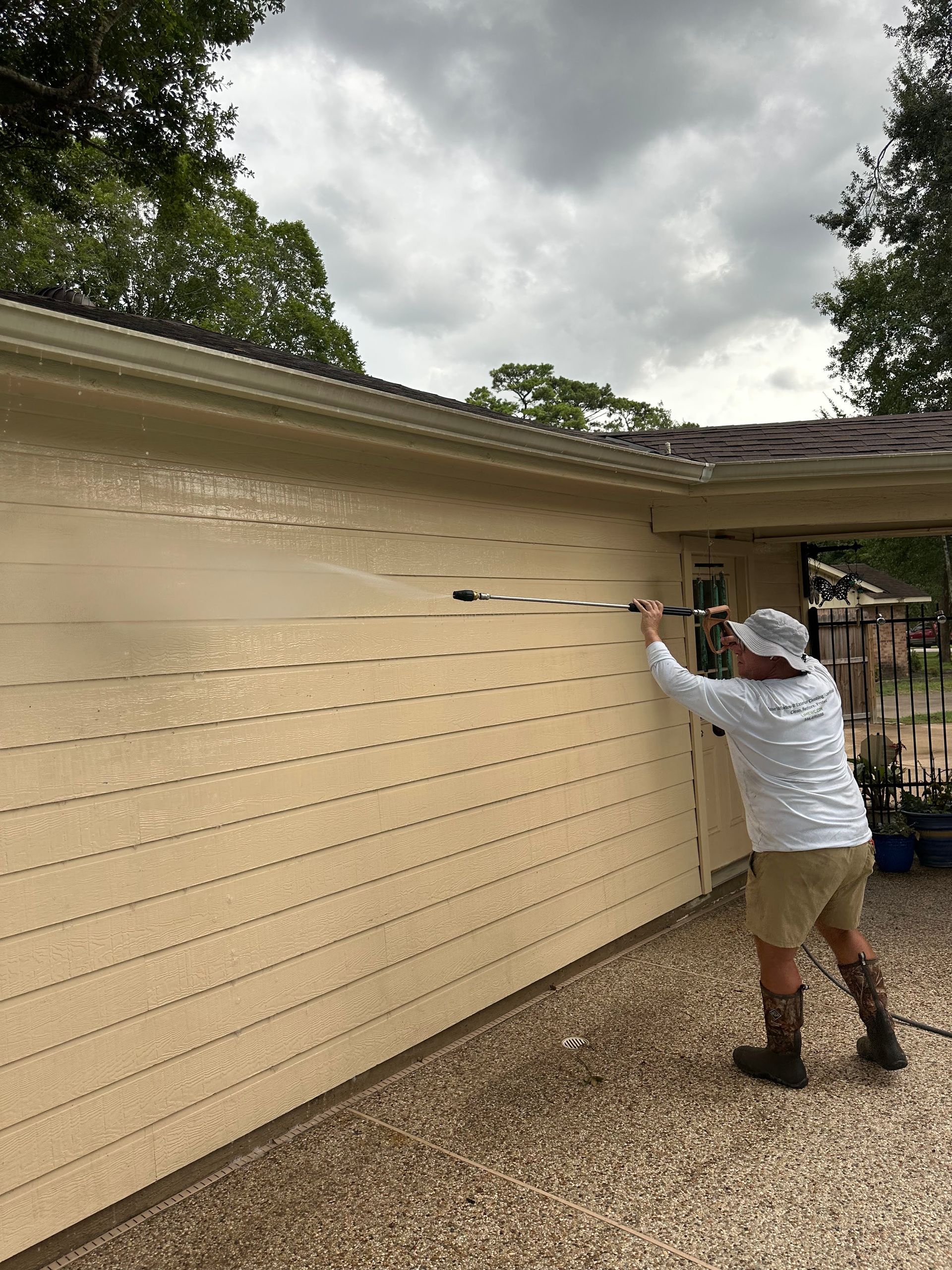Person painting a beige house exterior under a cloudy sky