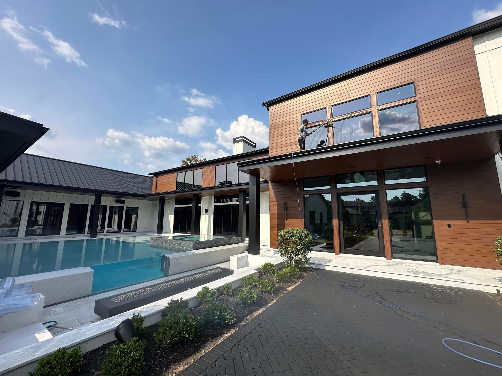 Modern house exterior with a swimming pool, large windows, and a paved driveway under a blue sky