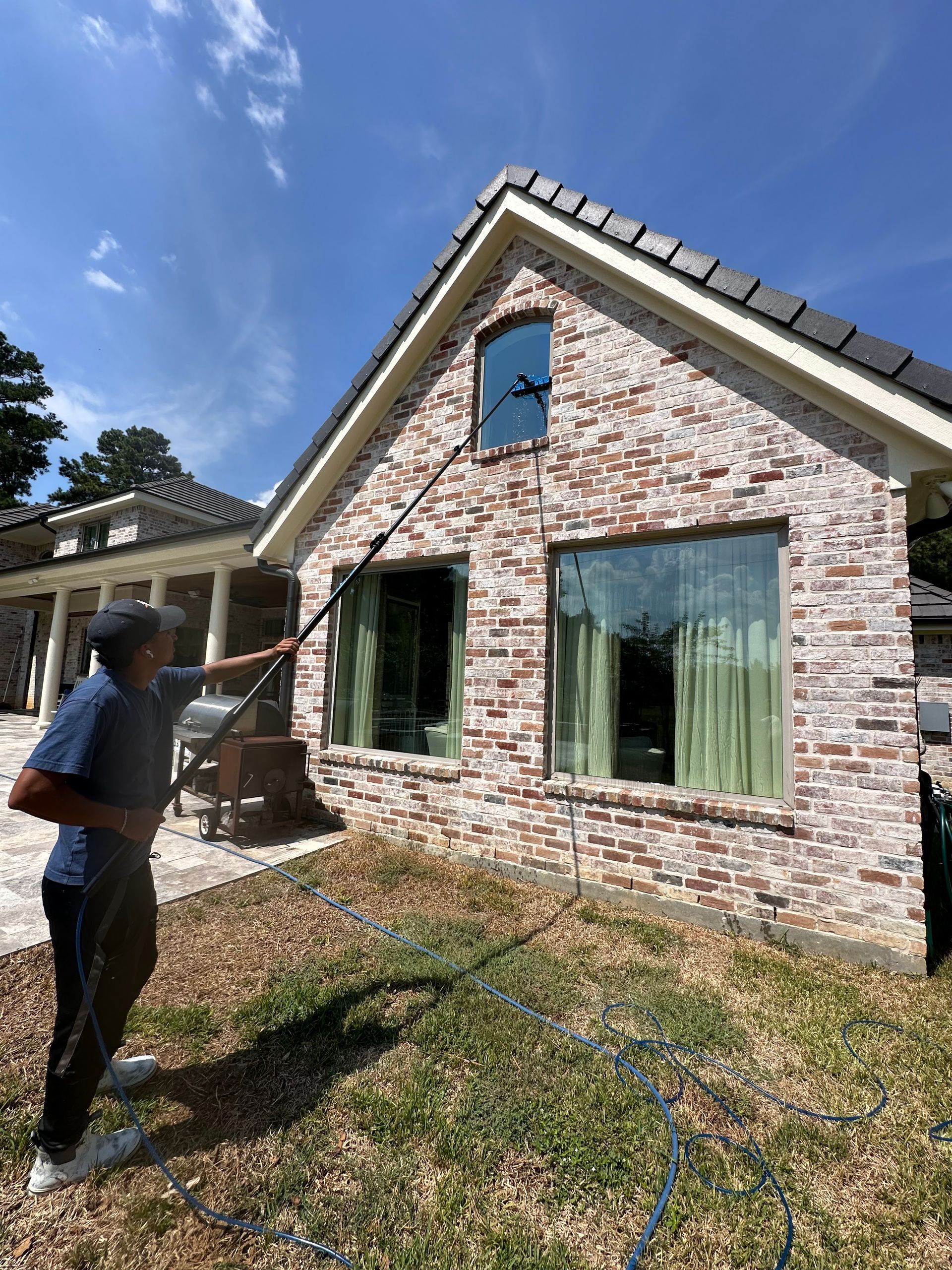 Person using a ladder to inspect the exterior of a brick house with open windows and blue sky.