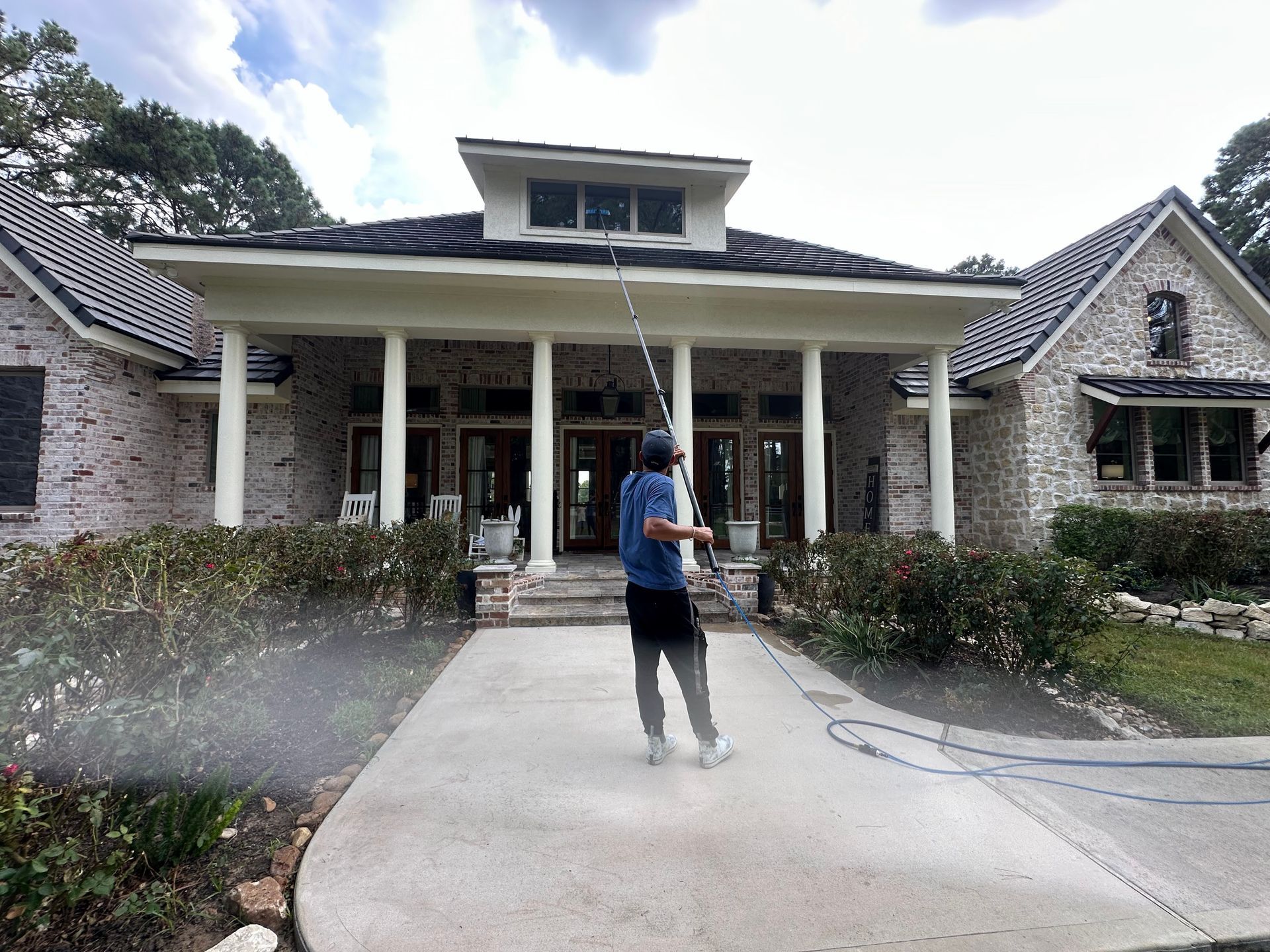 Person walking toward a stone house with a covered porch and flower beds.