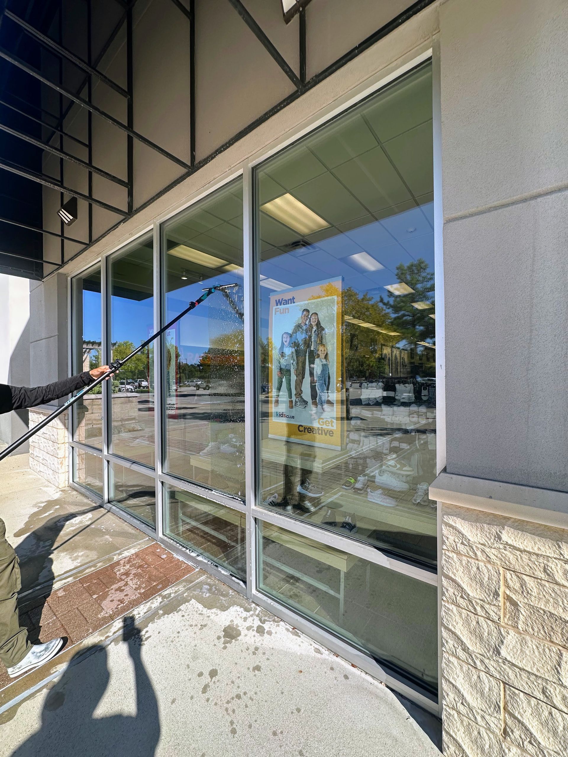 Storefront with large glass windows reflecting trees and sky, next to a stone column and sidewalk.
