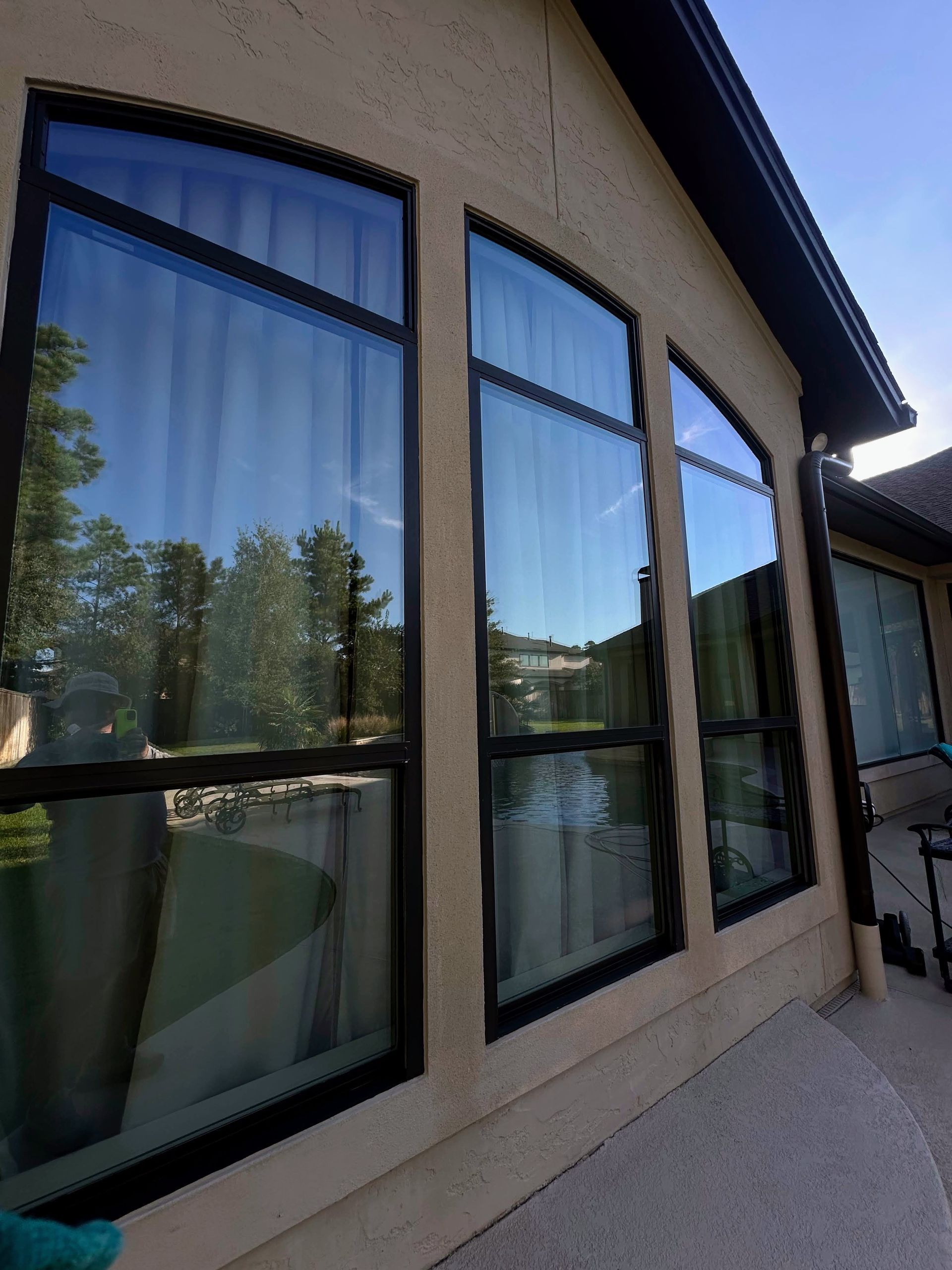 Tan house exterior with arched reflective windows along a sunlit patio