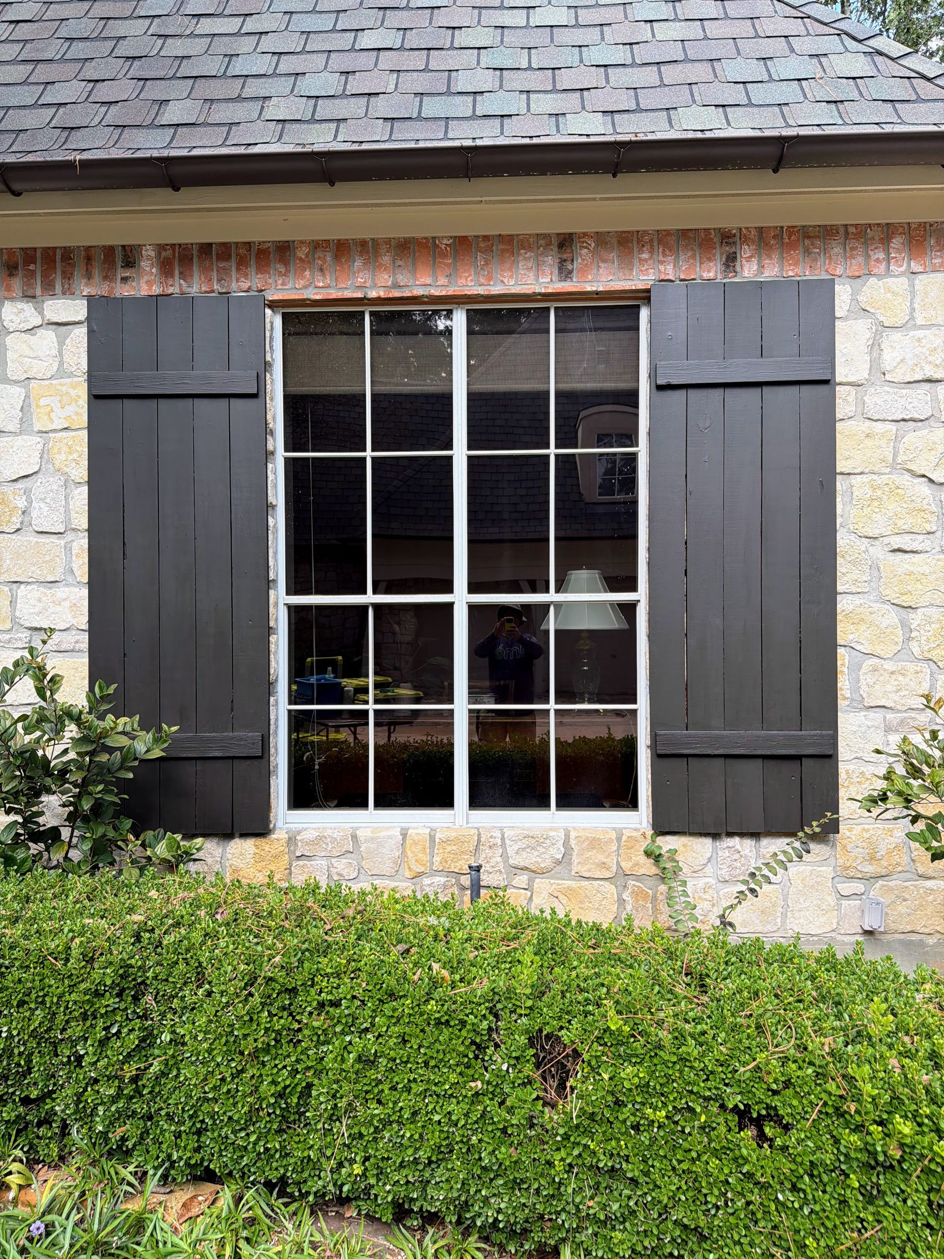 Stone house window with black shutters, white trim, and ivy in front