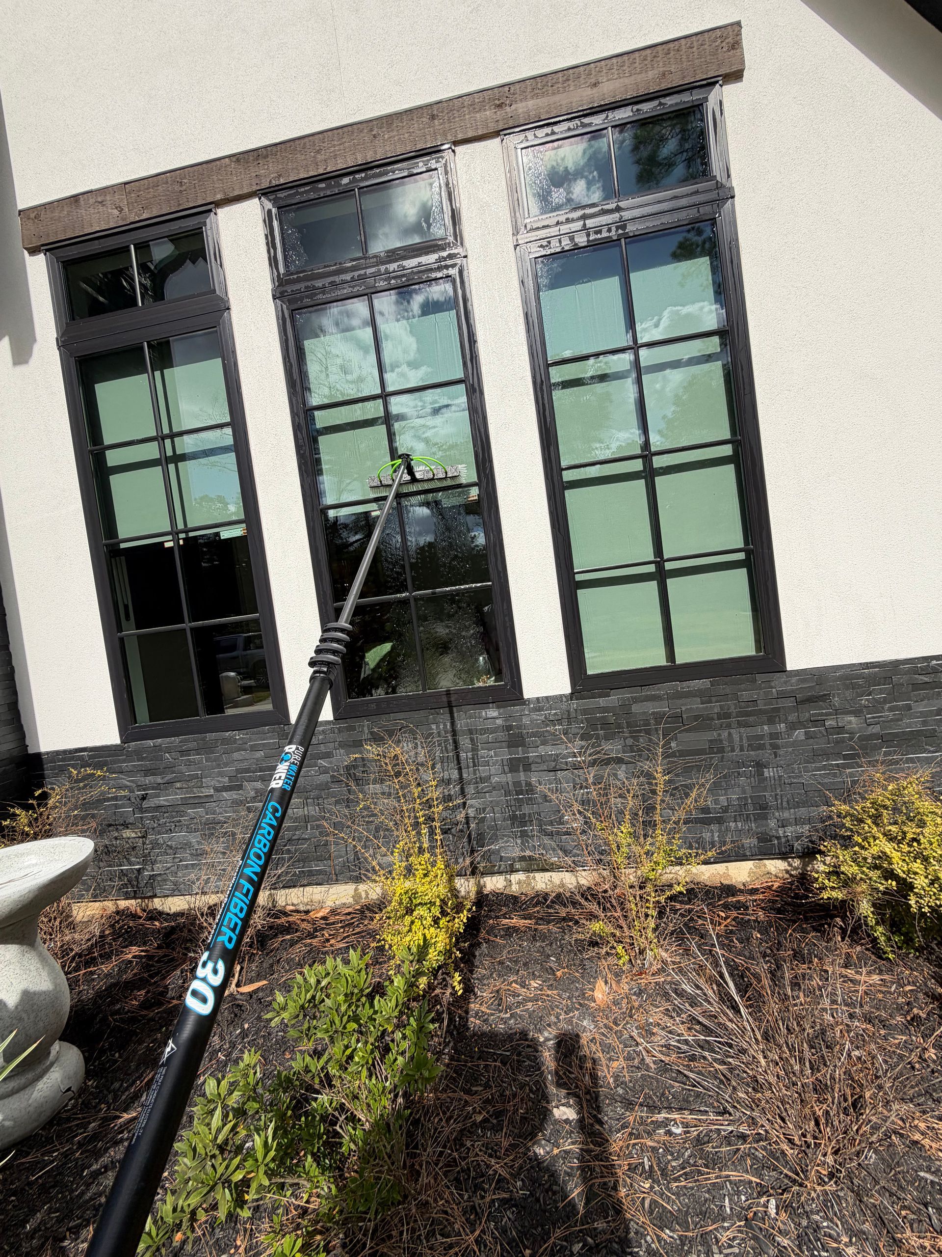 Window cleaning pole reaching up to tall building windows with a stone facade and landscaping below