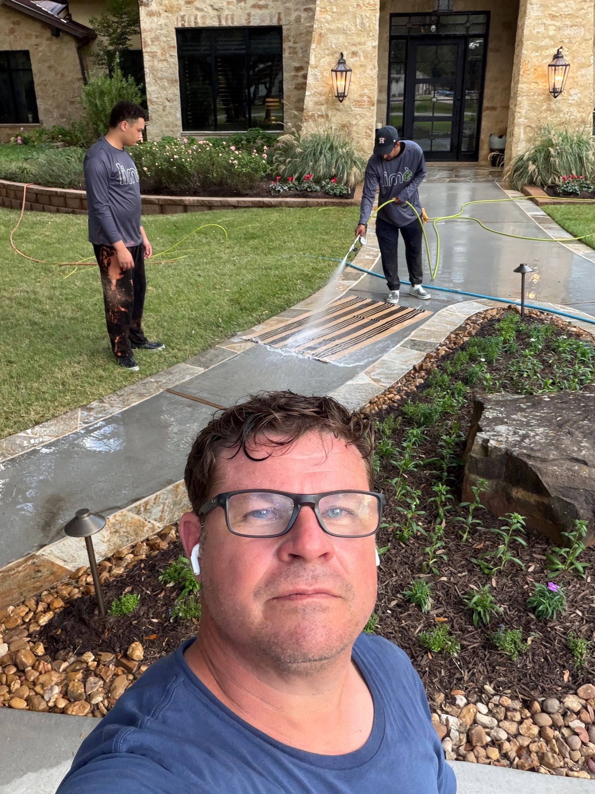 Three people work on a curved walkway outside a brick building, with one taking a selfie in the foreground.
