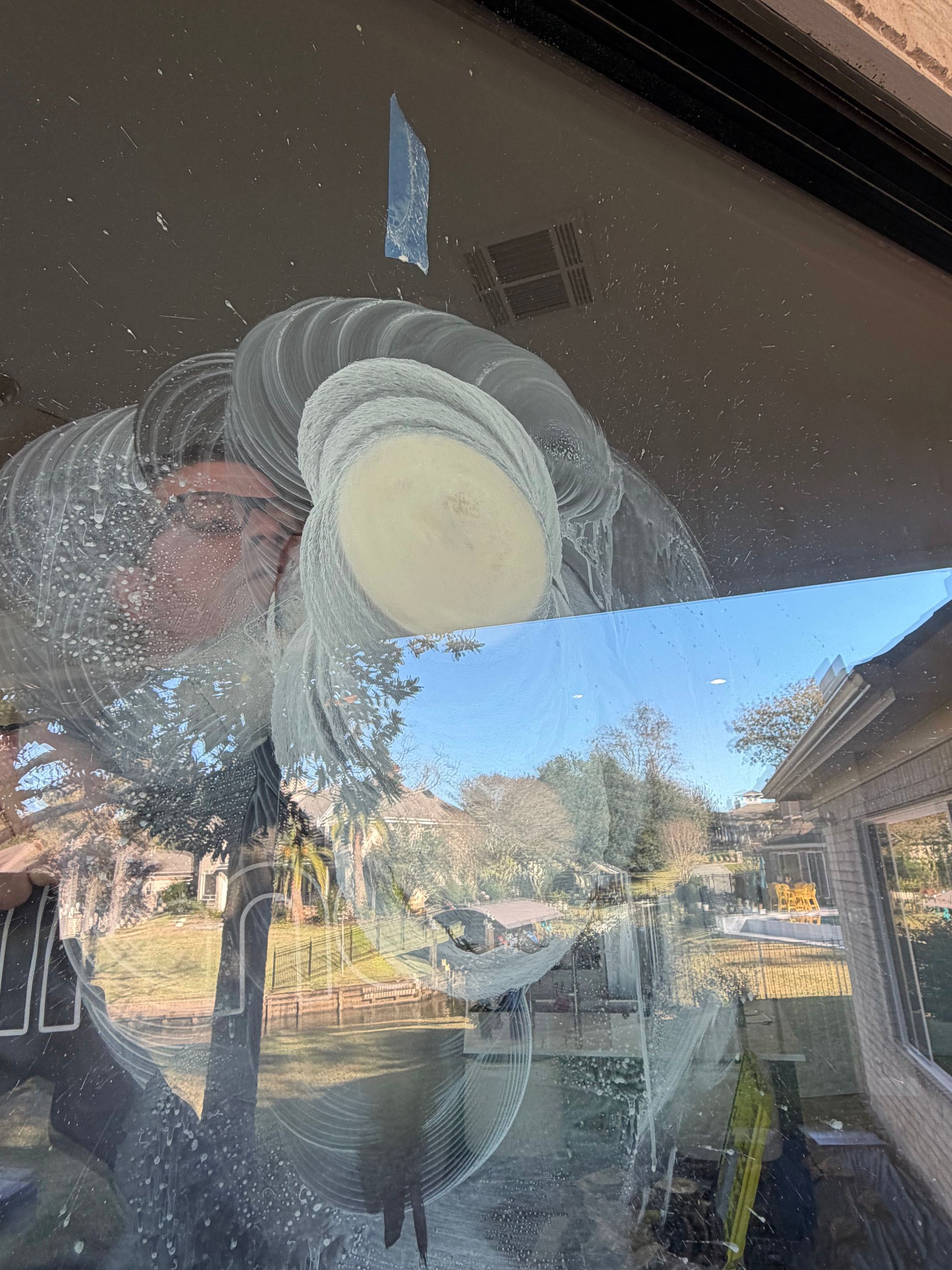 Reflection of a fan on a glass door, with a yard and house visible outside.