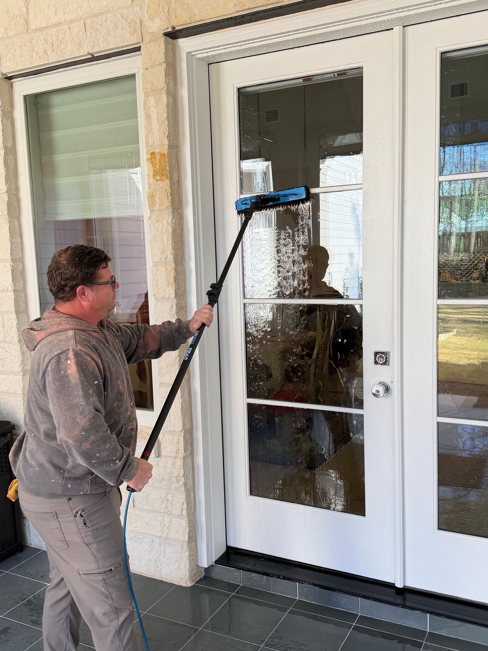 Person cleaning glass doors with a long-handled tool outside a building entrance.