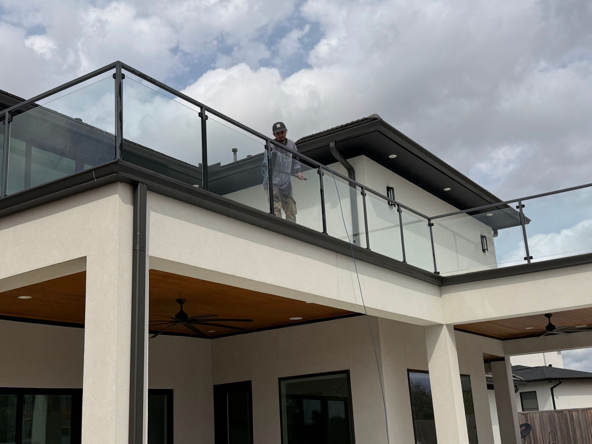 Person standing on a modern balcony with glass railings under a cloudy sky.