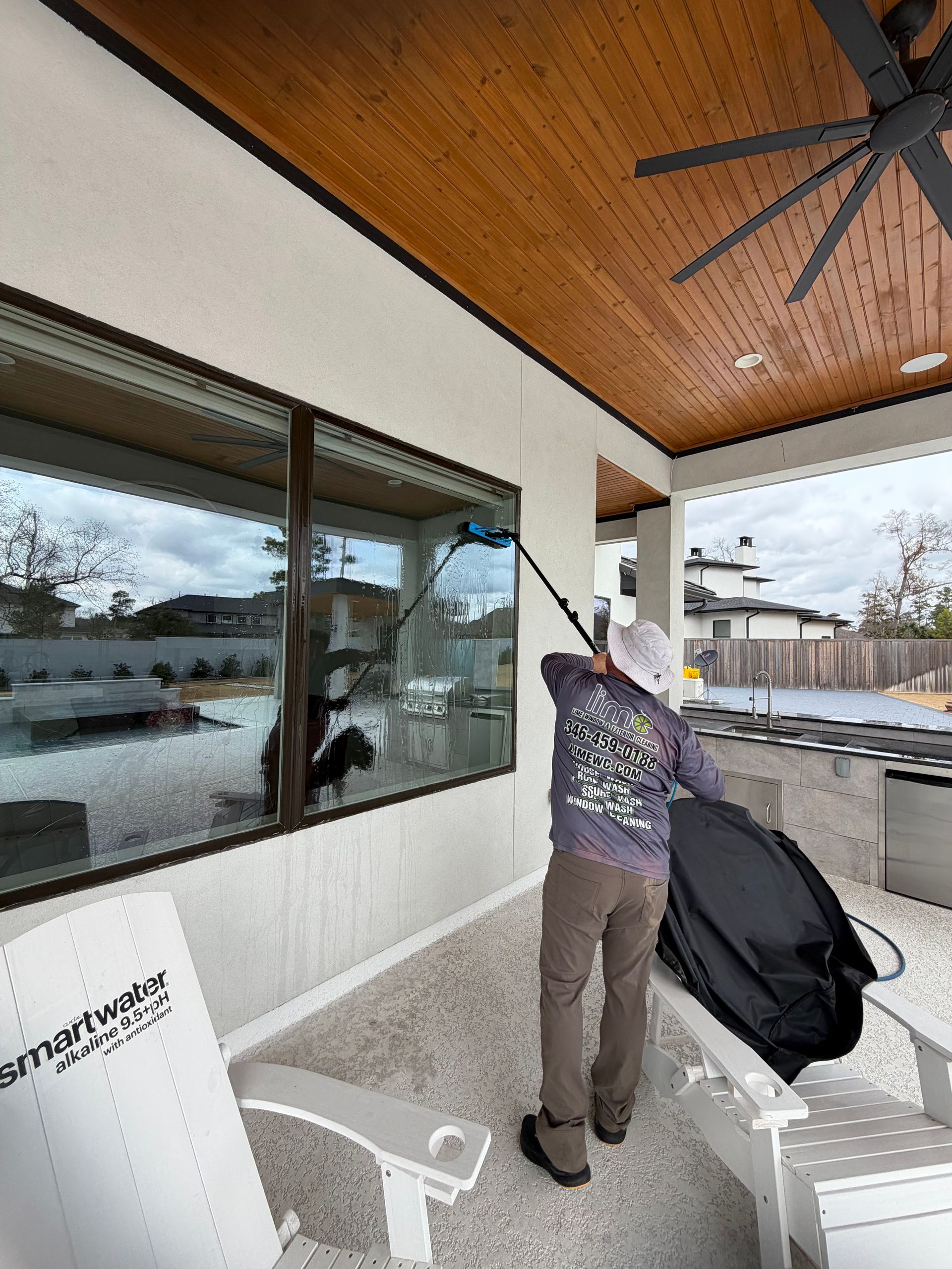 Person cleaning a patio with a leaf blower beside a windowed house and outdoor seating