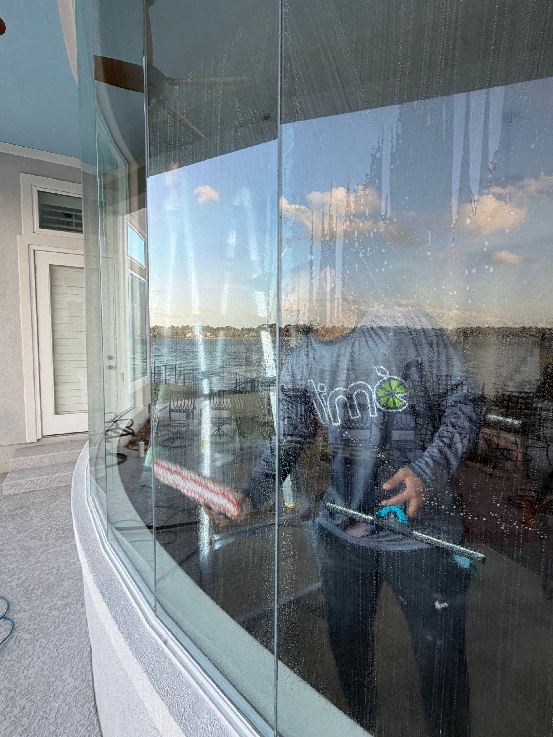 Two people reflected in a curved glass window, one in a blue jacket holding a device.