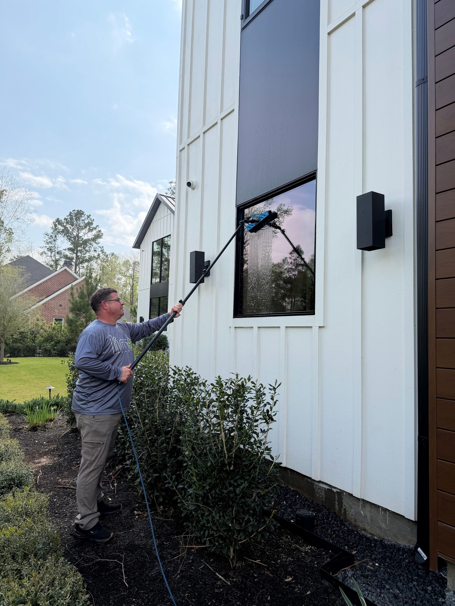 Person using a pole tool to clean an upper window on a white house exterior.