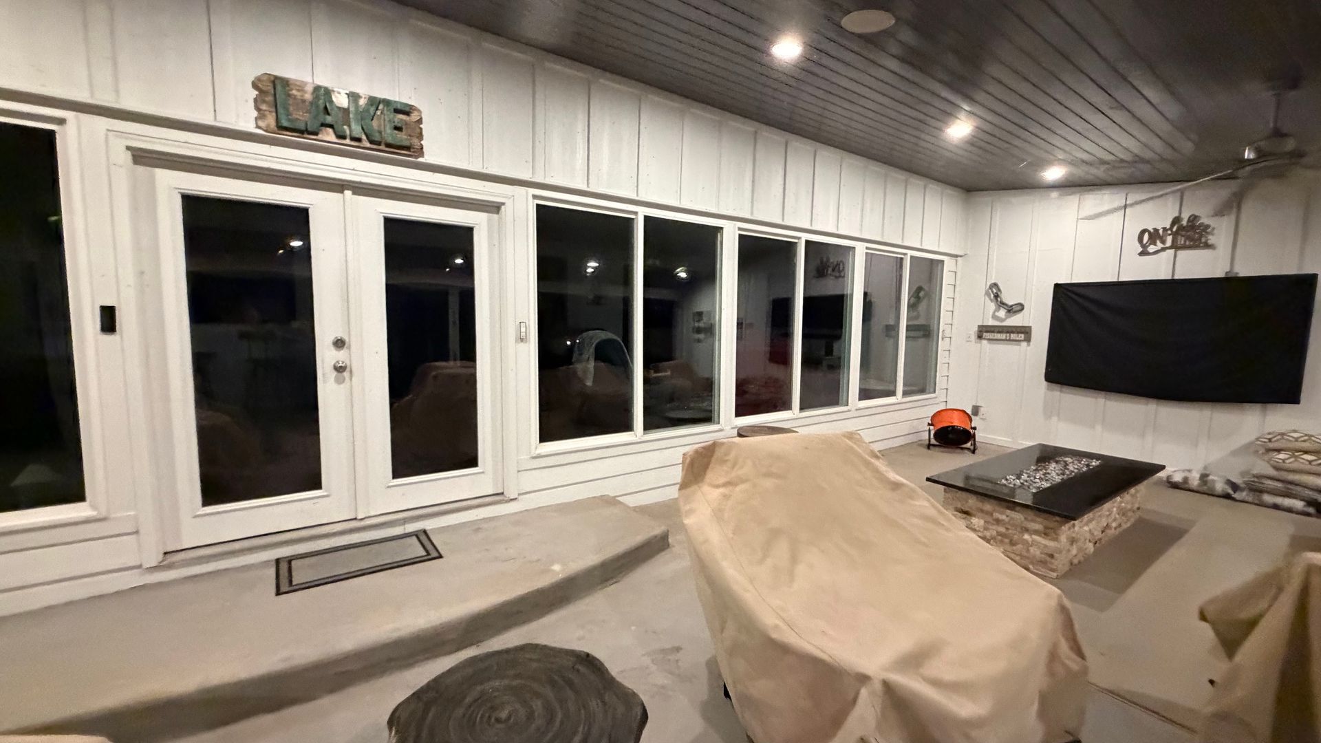 Modern living room with white French doors, a large TV, and furniture covered with protective sheets.