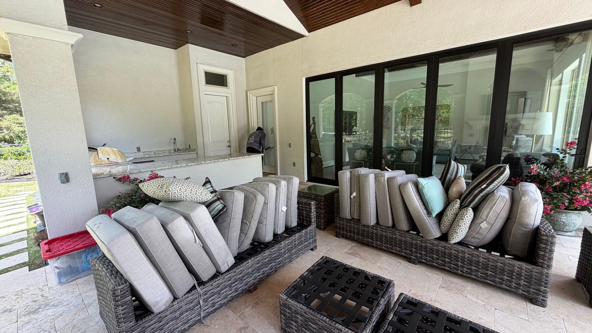 Covered patio with wicker sofas, striped cushions, and glass doors opening to a house