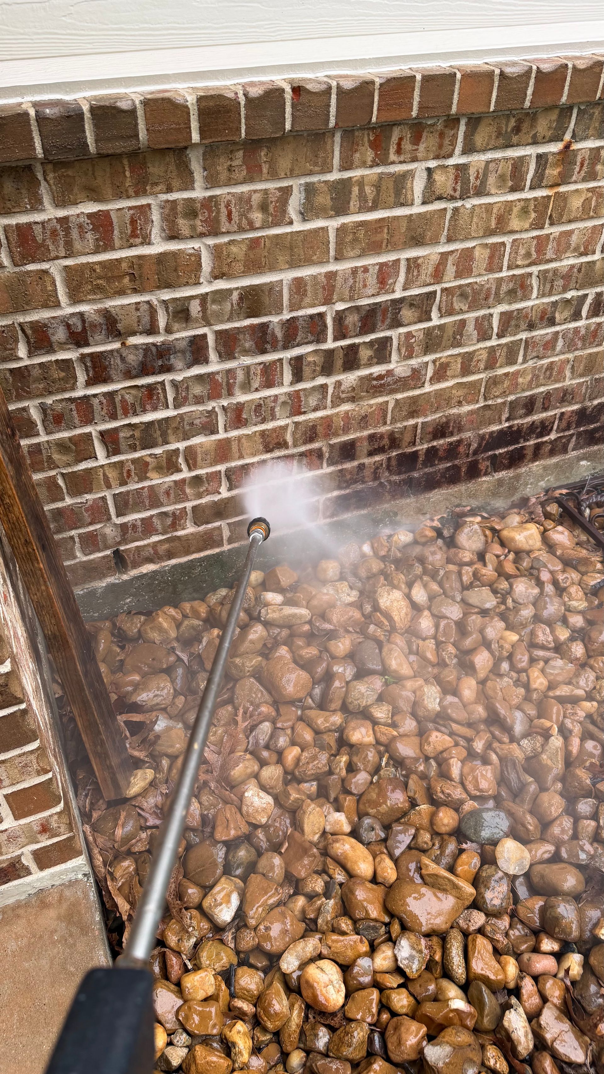 Pressure washing a brick wall beside a pebble bed