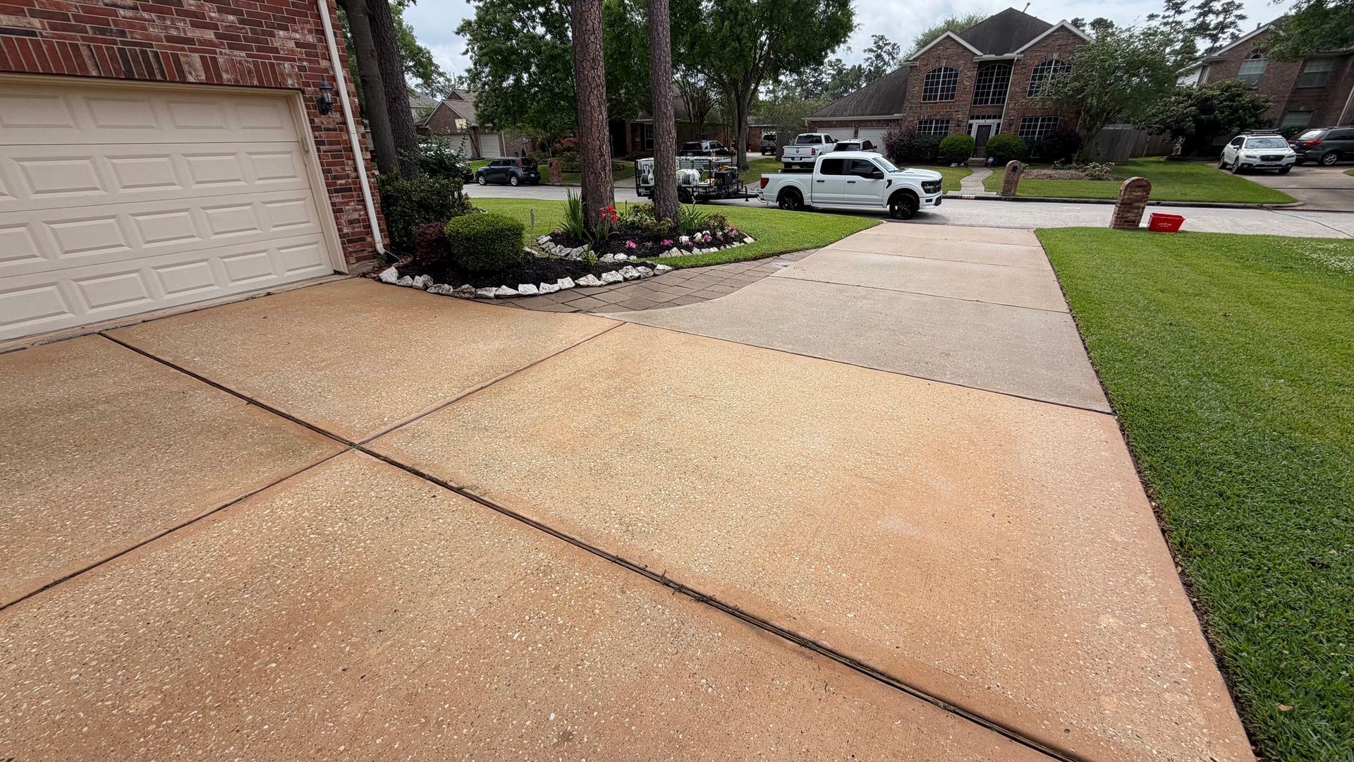 Wet driveway and sidewalk beside a brick garage in a suburban neighborhood.