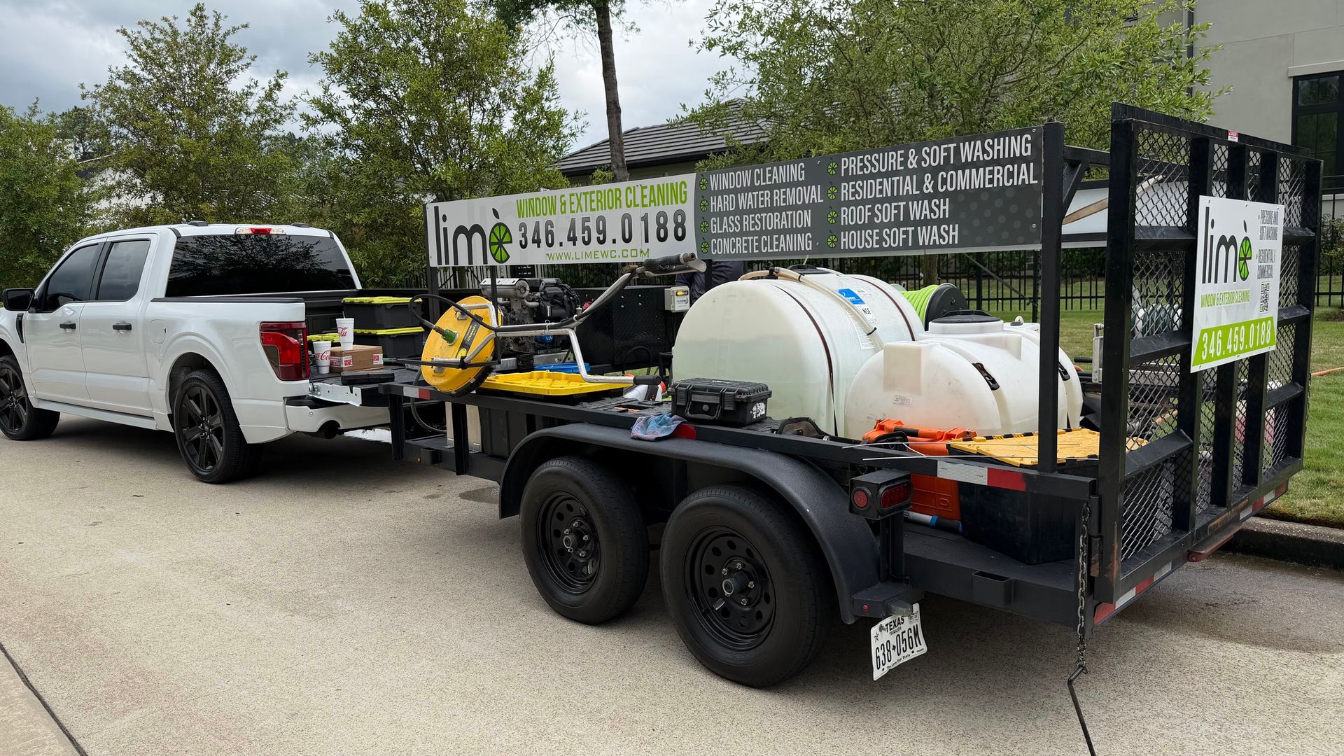 White SUV towing a black utility trailer with a water tank and equipment in a driveway