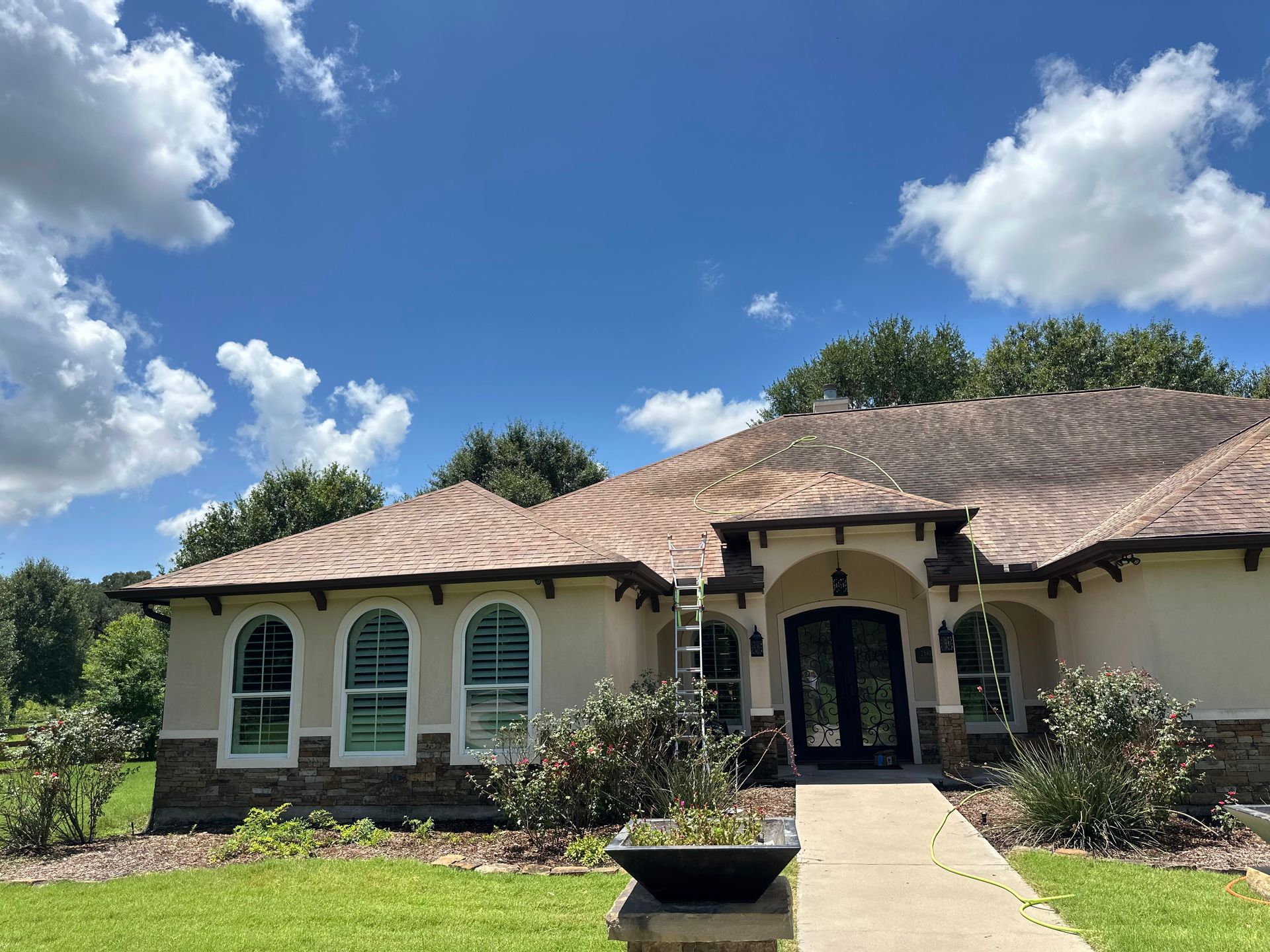 Single-story beige house with arched windows, dark front door, and a curved walkway under a blue sky