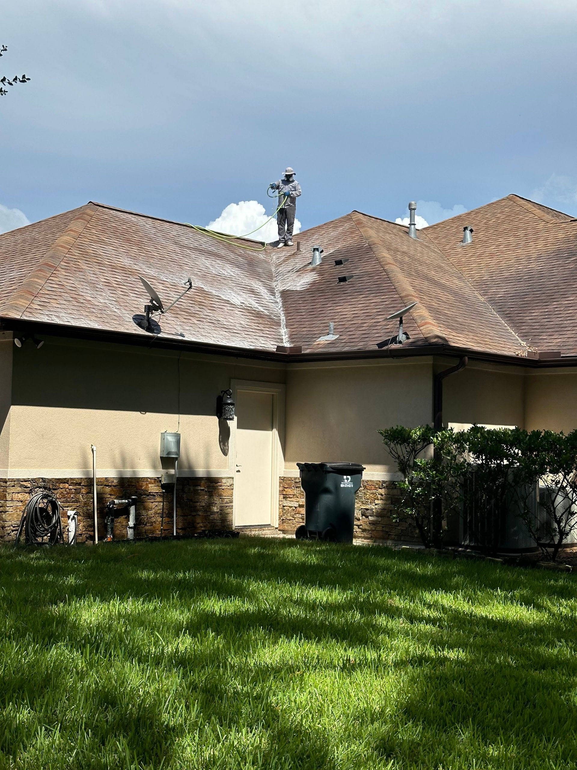 Backyard with green lawn, beige house wall, and wavy brown shingle roof under a blue sky