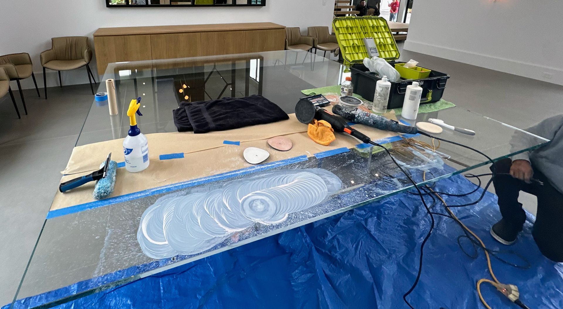 Workshop table with a blue tarp, tools, wires, and a chalk-drawn oval design in a room.
