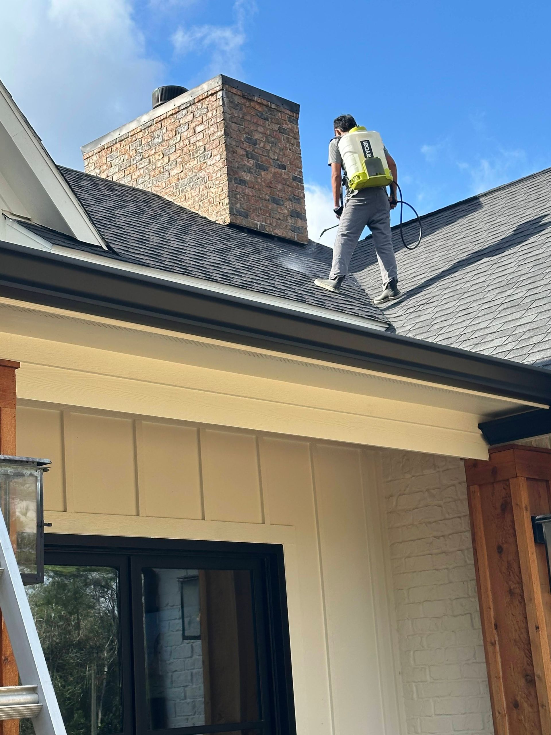 Worker on a shingled roof inspecting a chimney on a house under a blue sky