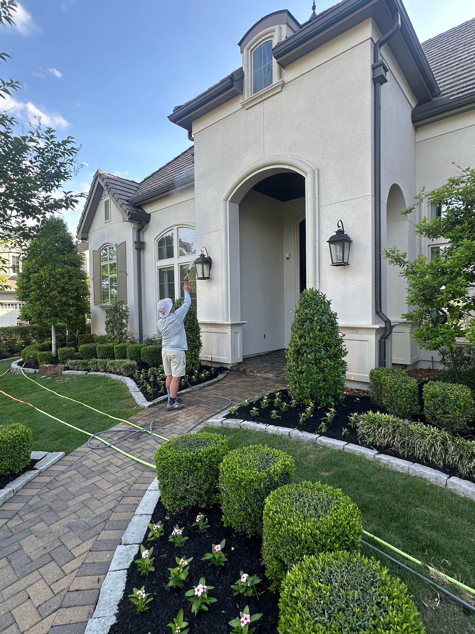 Elegant stucco house entrance with arched doorway, manicured hedges, and stone walkway under a blue sky