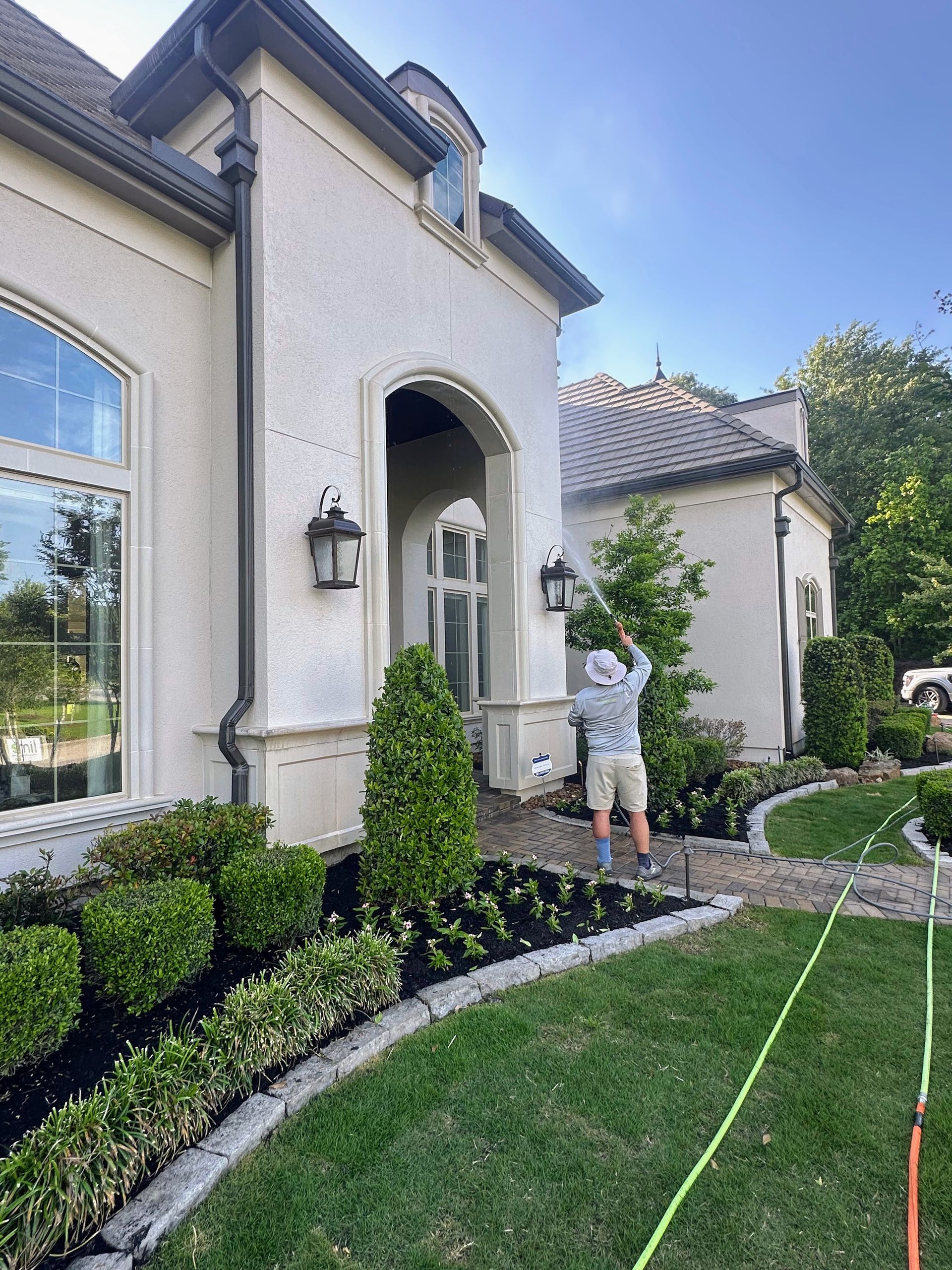 Boy standing by a large stucco house entrance with trimmed hedges and a green lawn.