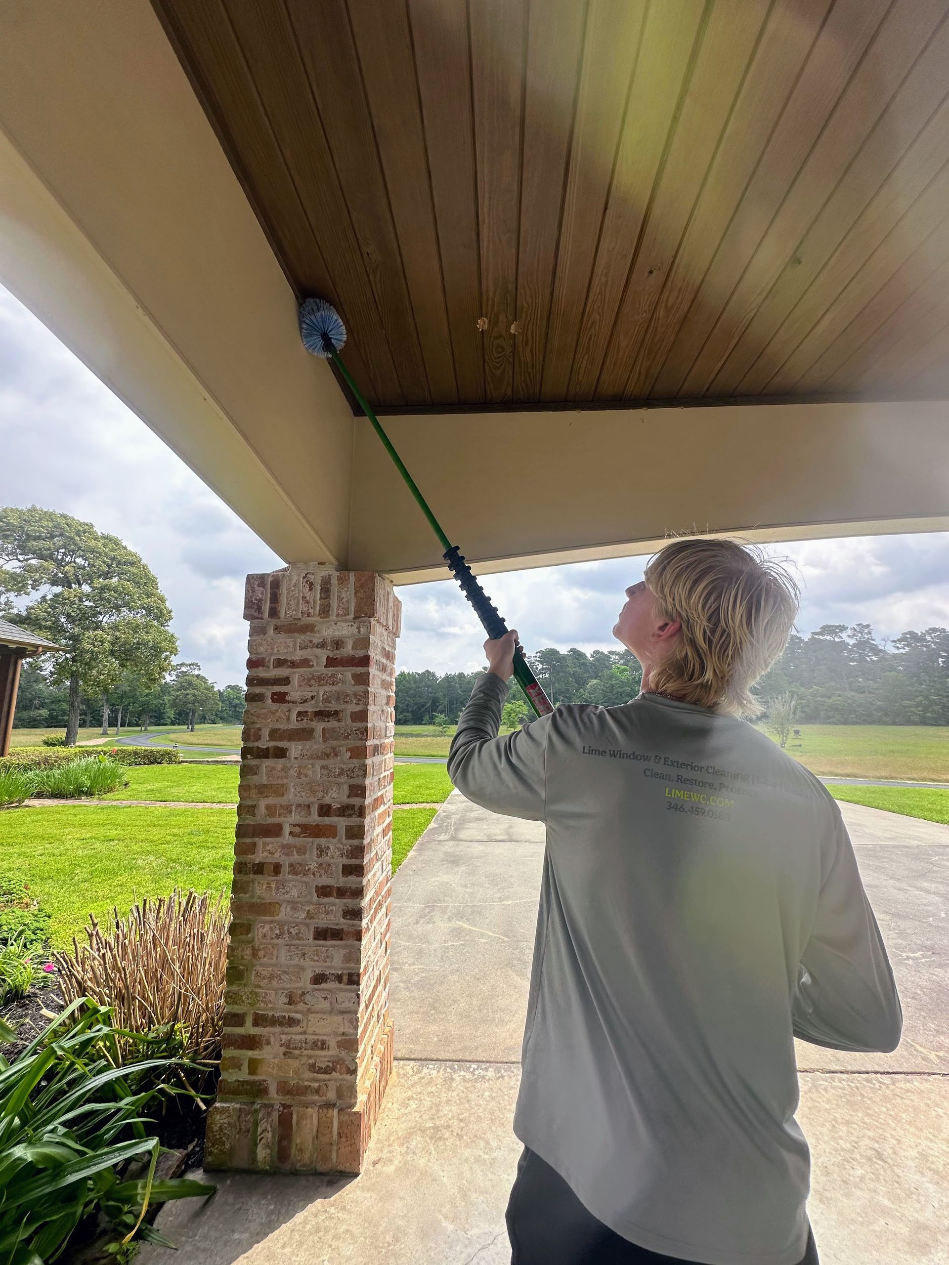 Person pressure-washing a house’s porch ceiling under a covered patio