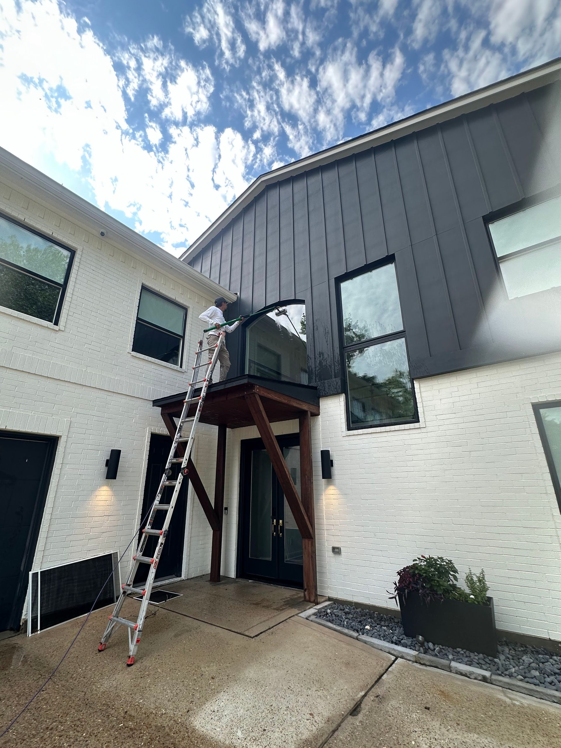 Worker on ladder repairing a modern building’s upper entrance canopy