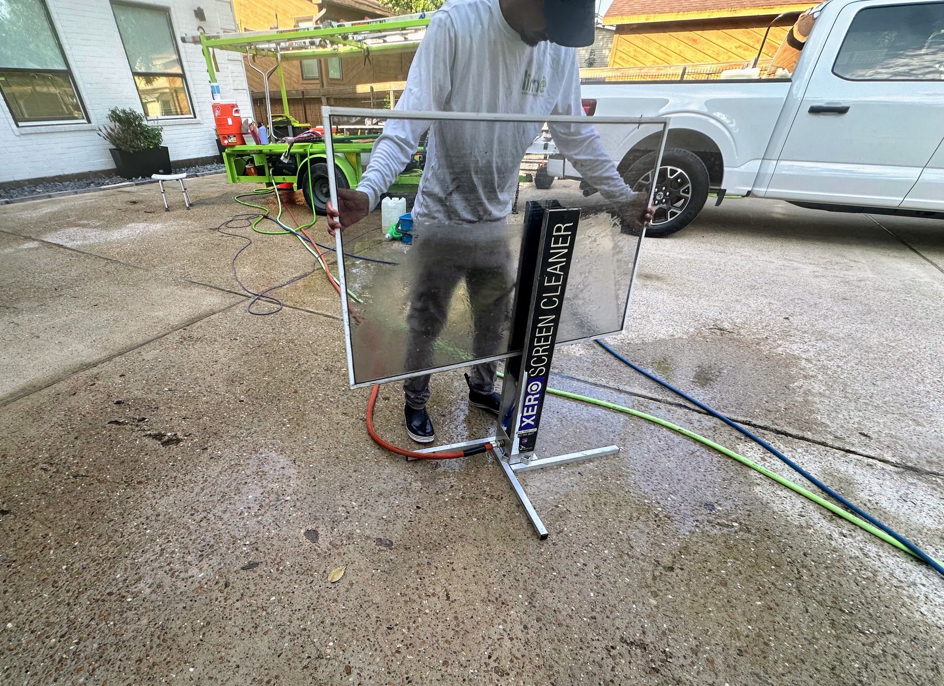 Person pressure-washing a concrete driveway beside a white van and hoses, with water spraying around.