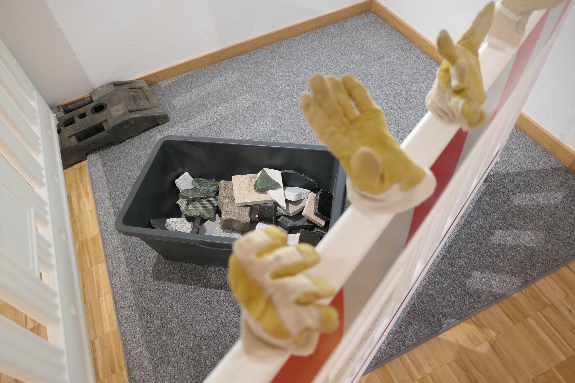 Handschuhe auf einer Baustellenabsperrung und eine Wanne mit viele Steinen zum Bauen.