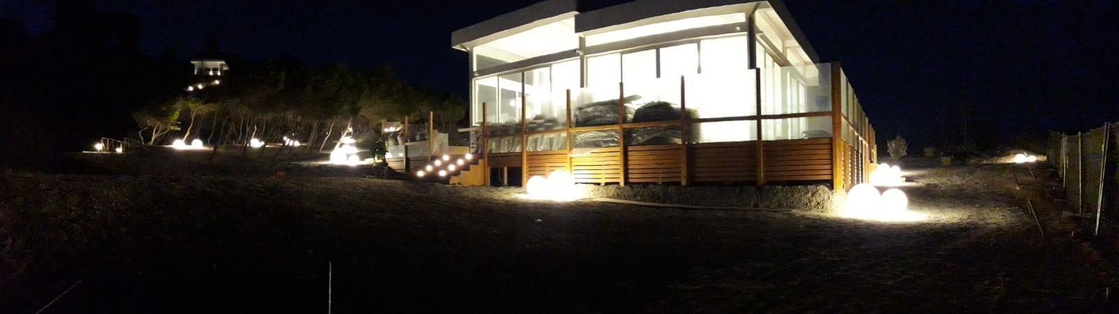 Un edificio moderno con un'illuminazione interna intensa di notte. Luci a terra illuminano l'esterno.