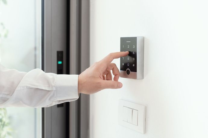 Mano che inserisce il codice su un sistema di sicurezza con tastiera montato su una parete bianca vicino a una finestra.