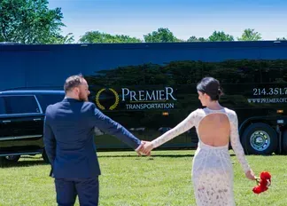 A bride and groom are holding hands in front of a bus.