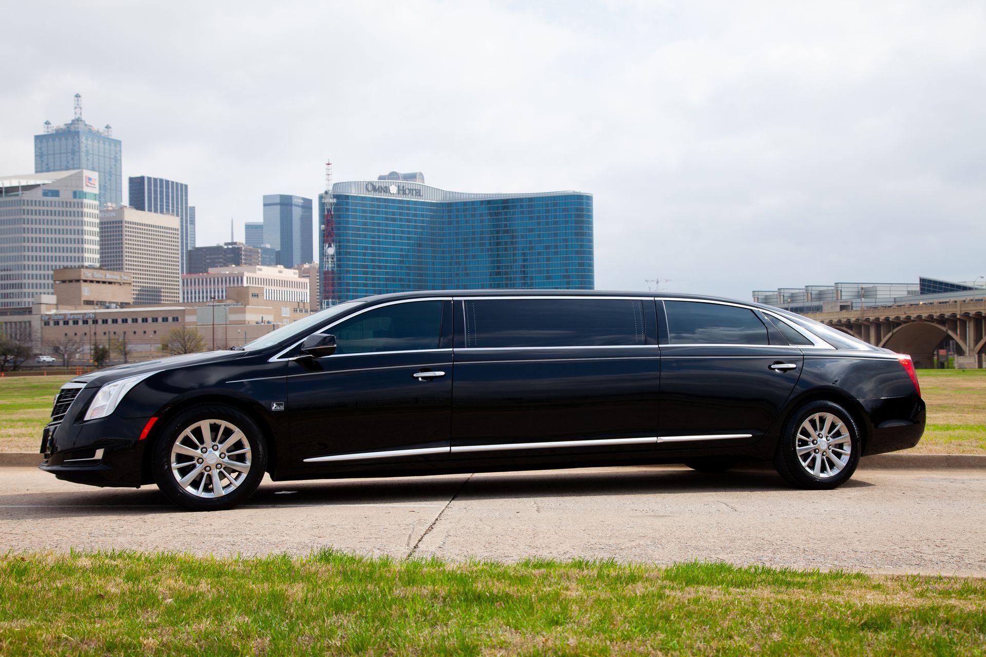 A black limousine is parked on the side of the road in front of a city skyline.
