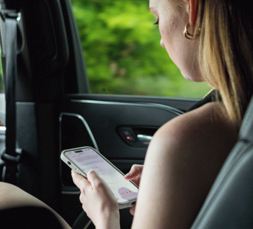 A woman is sitting in the back seat of a car looking at her cell phone.