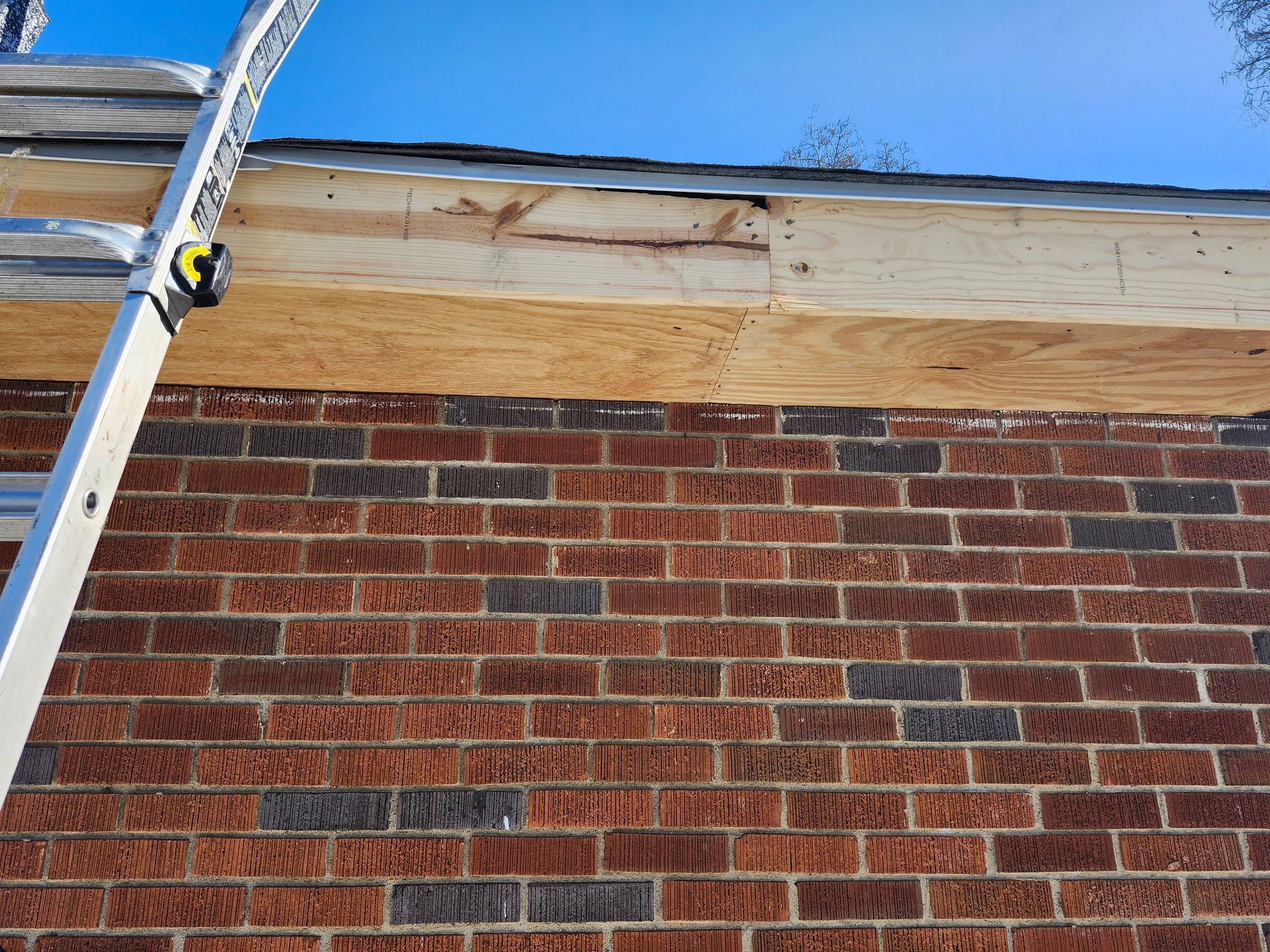Ladder leaning against a brick wall beneath a wooden roof edge under a blue sky