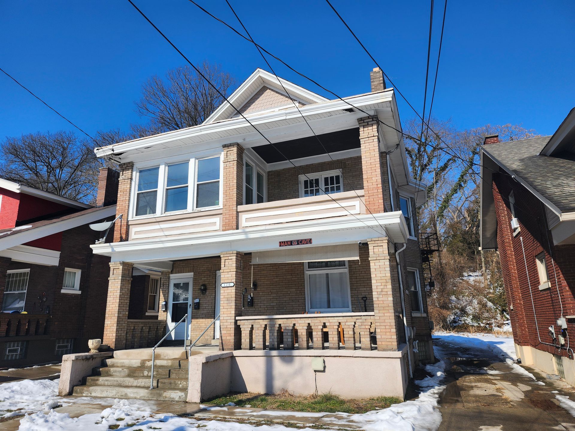 Two-story stone house with a porch and large windows, snow on the ground, under a bright blue sky