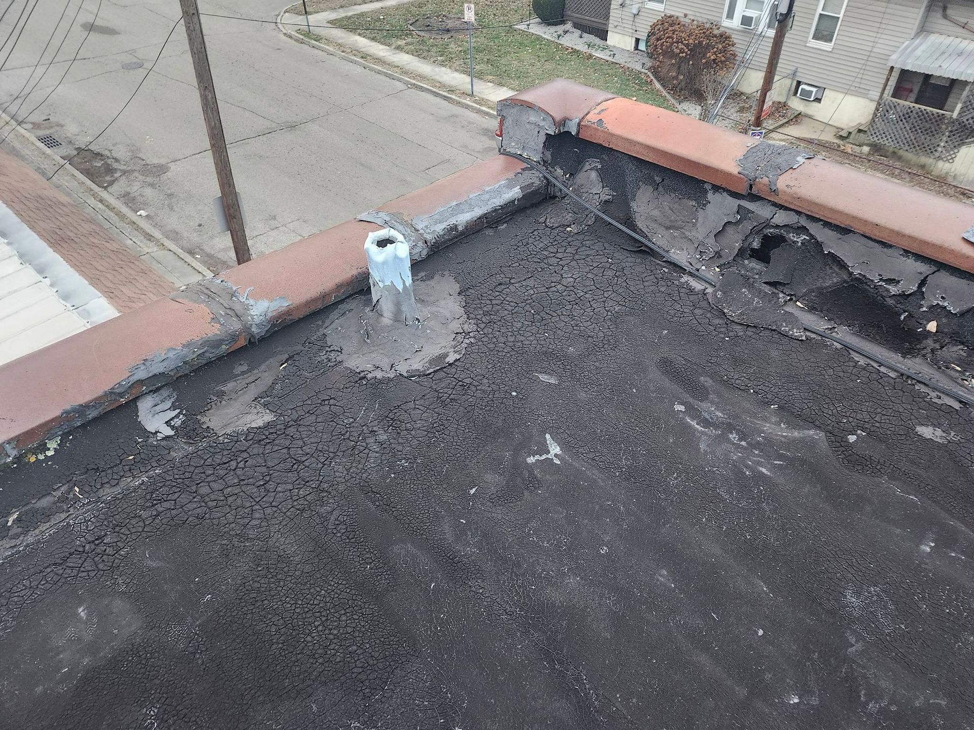 Flat rooftop with gravel surface, red coping, and a white vent pipe near the edge.