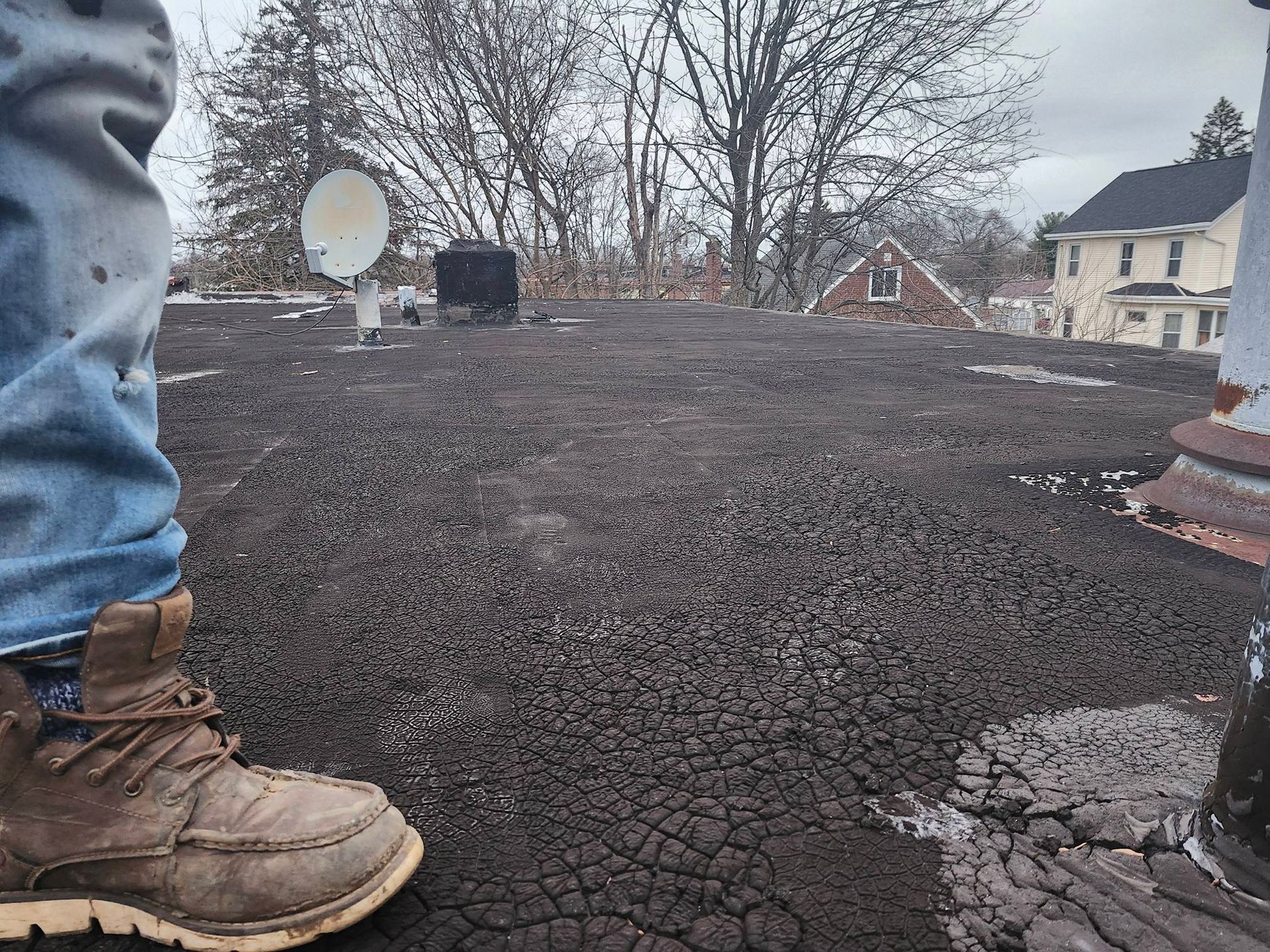 Boot on cracked gravel roof with satellite dish and houses in the background
