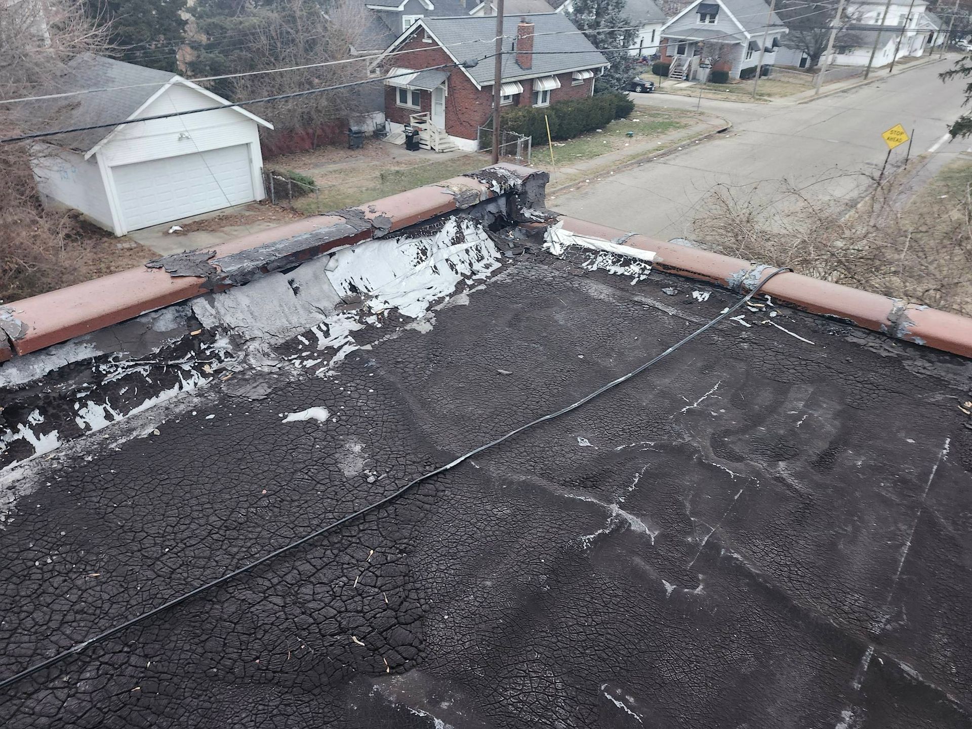 Rooftop with peeling black coating overlooking houses and a street below