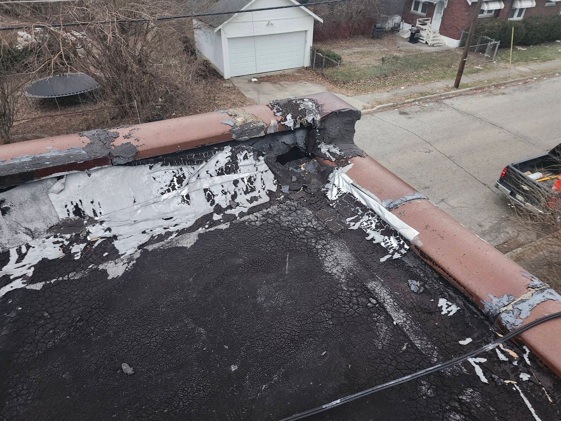 Roof shingles and flashing damaged around a chimney, with a residential street and garage in view.